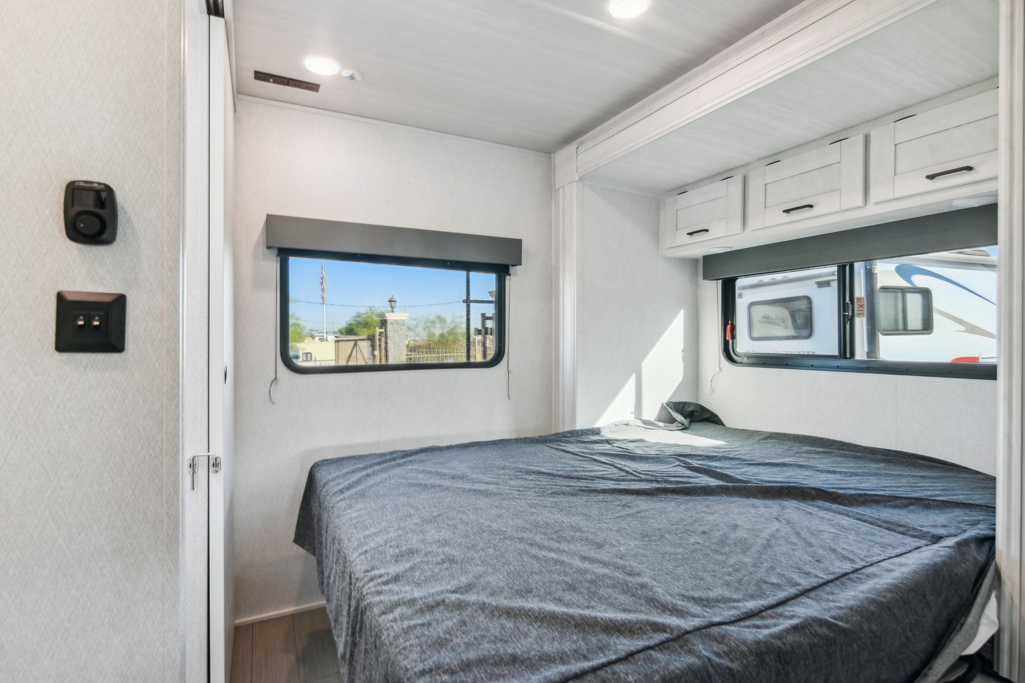 Bright RV rental bedroom with a neutral-toned bed, multiple windows, and overhead cabinets, designed for comfortable travel.. Forest River East to West Entrada 2024
