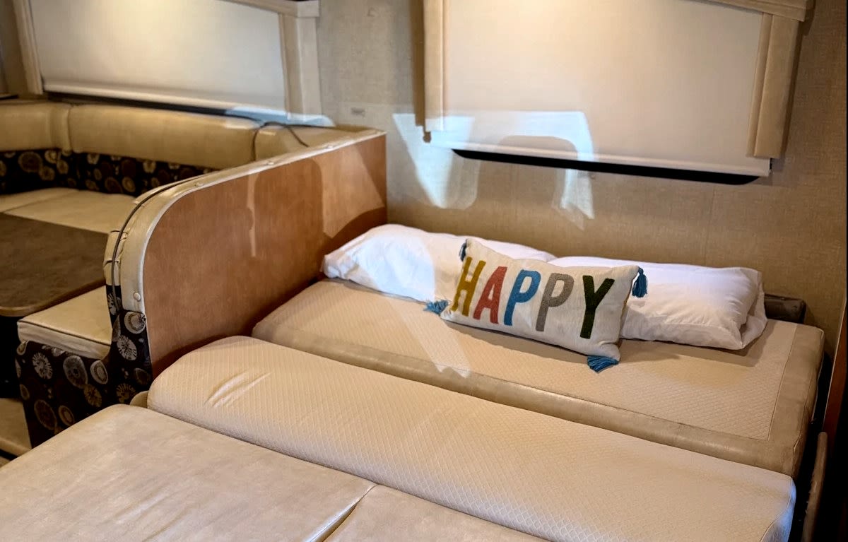 RV rental interior: Dinette seating on the left, and a bed with a 'HAPPY' pillow on the right.. Winnebago Minnie Winnie Premier 2015