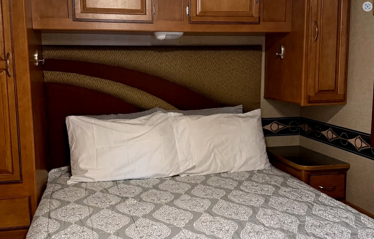 RV rental bedroom with a bed, white pillows, patterned comforter, wooden headboard, and overhead cabinets.. Winnebago Minnie Winnie Premier 2015