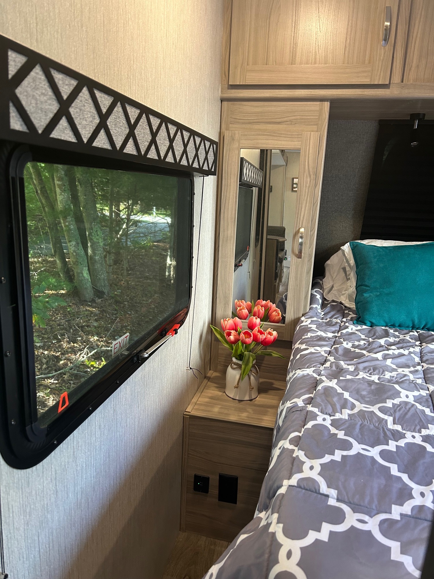 Cozy RV rental bedroom with a patterned comforter, fresh tulips, and a window view of lush trees.. Coachmen Freedom Express 287 BHDS 2021