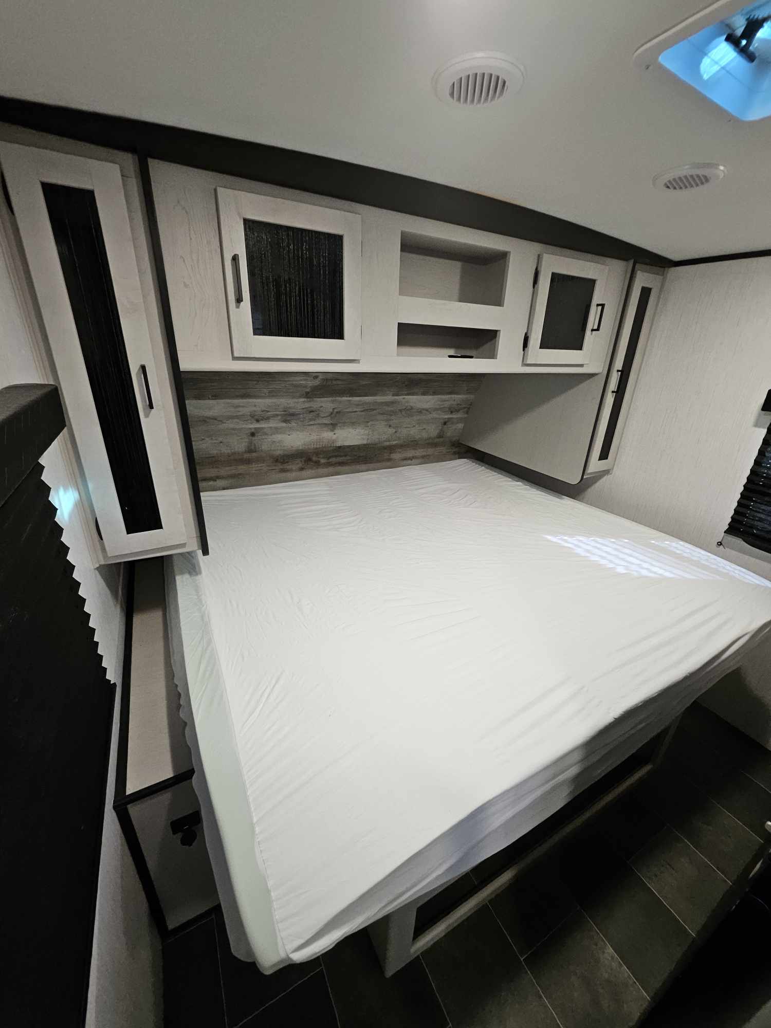 RV rental bedroom with a large white bed, wooden headboard, and modern overhead storage. Bright, clean interior awaits.. Heartland mallard 2022