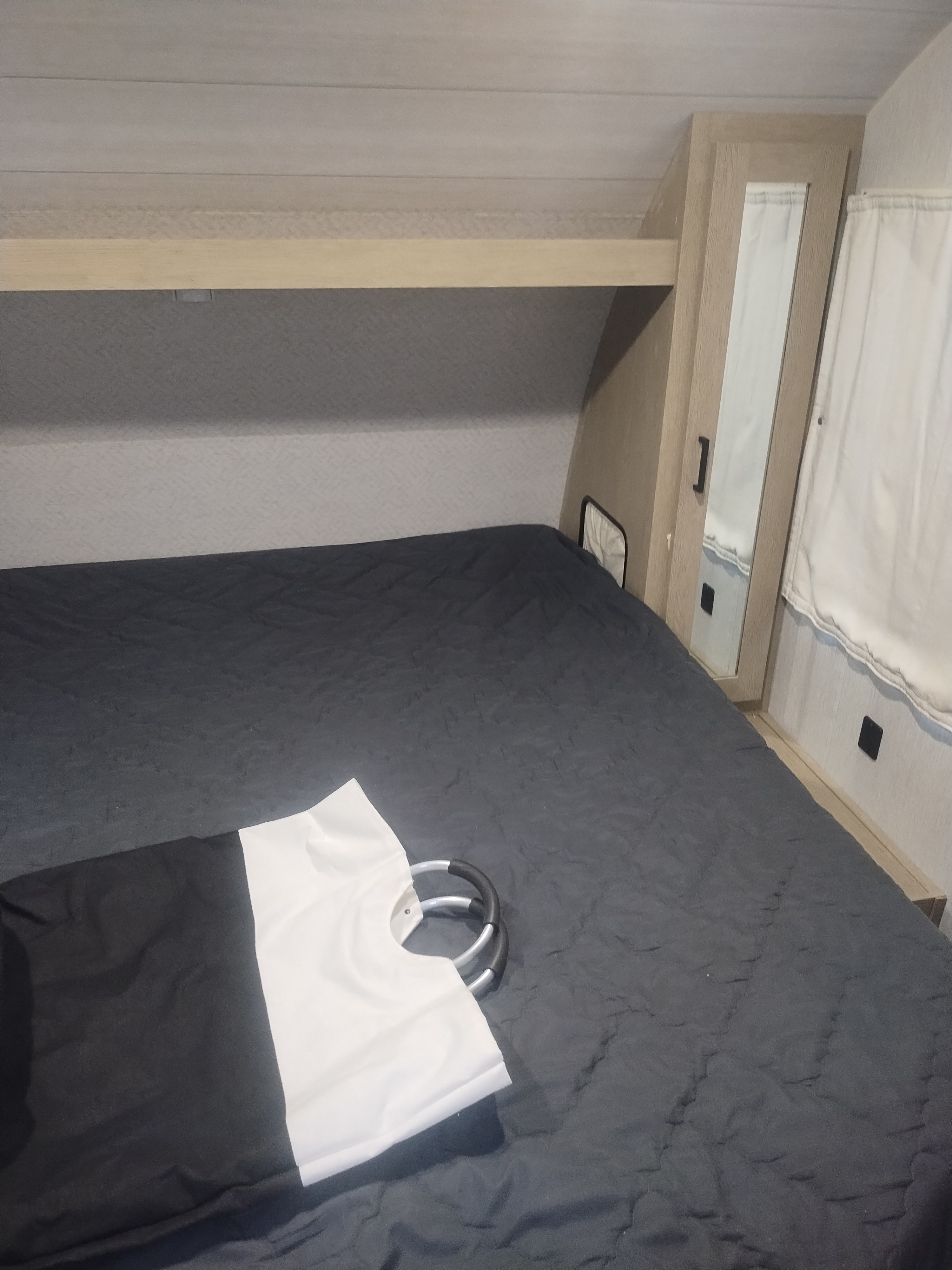 RV rental bedroom: a cozy interior with a dark bed, overhead shelf, mirrored wardrobe, and black & white laundry bag.. Forest River Salem 2024