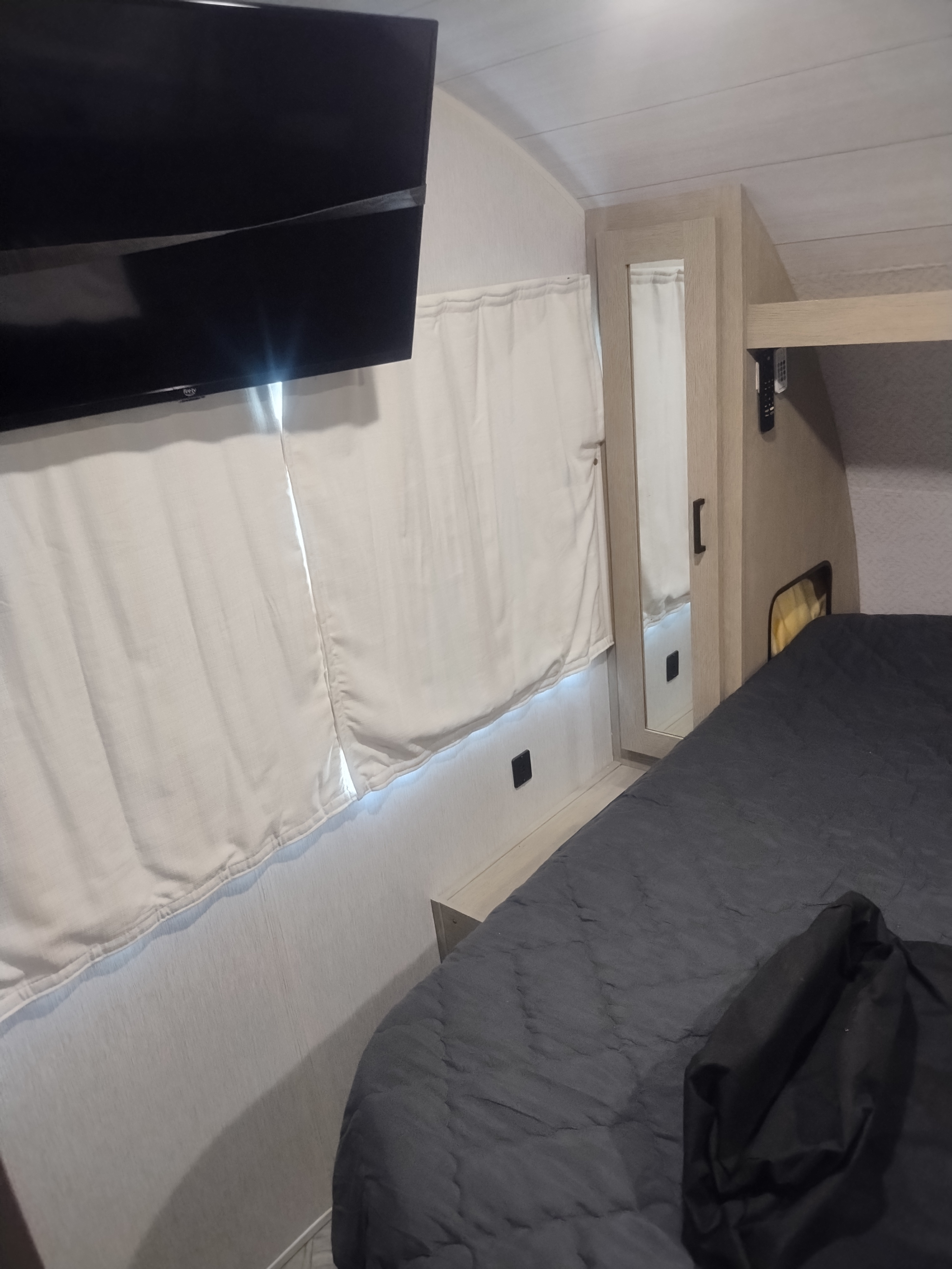 Cozy RV rental bedroom with a mounted TV, bed with dark gray bedding, and built-in storage. Ideal for your travel adventures.. Forest River Salem 2024