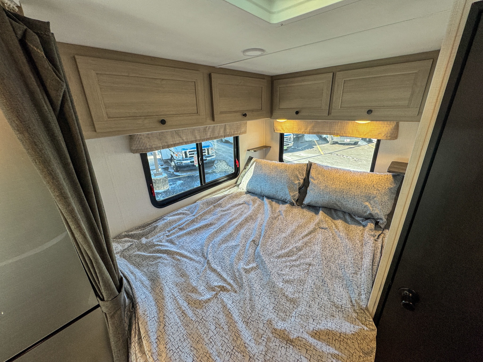 Cozy RV rental bedroom with a comfortable bed, ample overhead cabinets, and windows showcasing the outside.. Forest River Sunseeker 2024