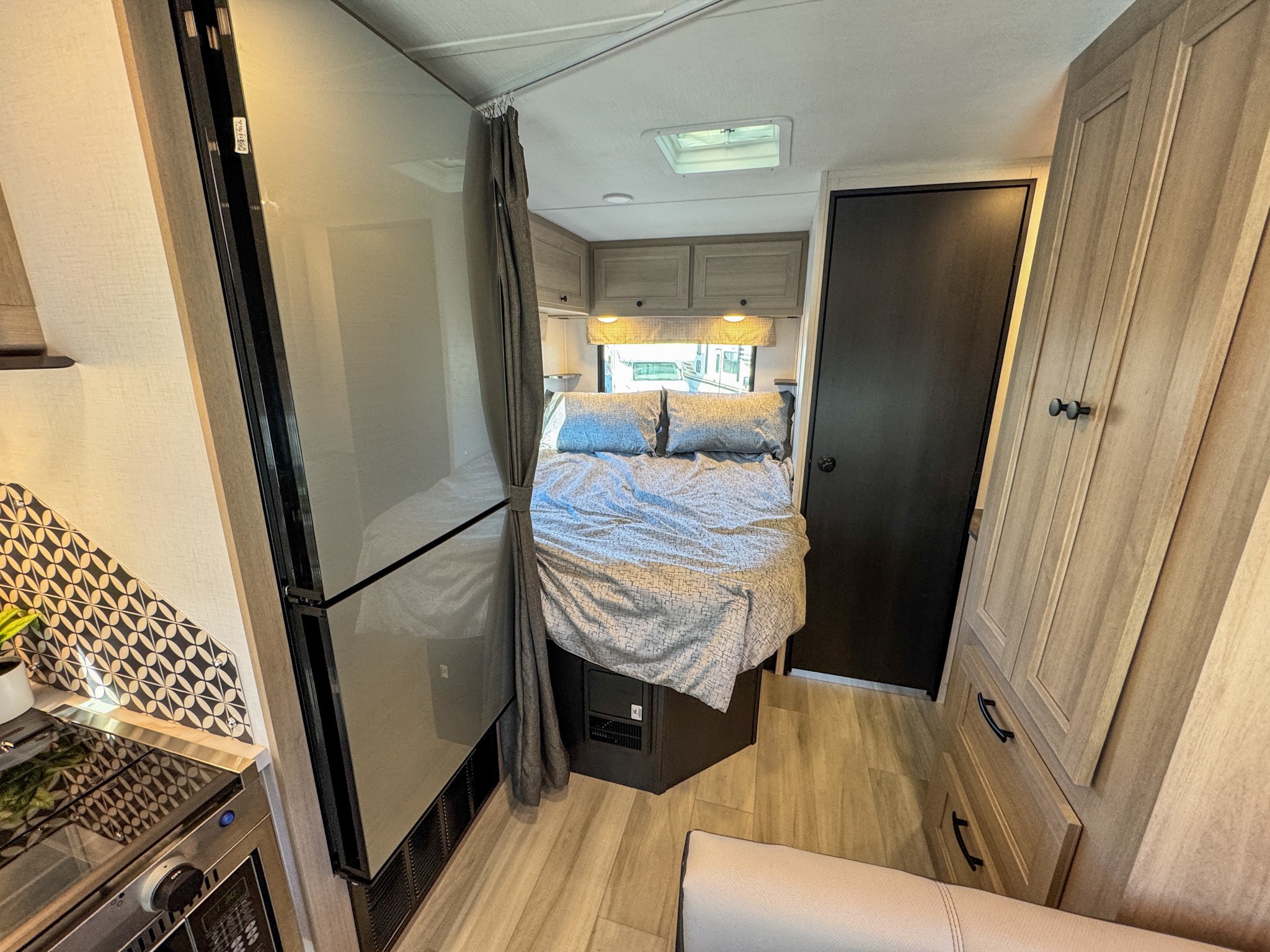 Cozy RV rental interior showcasing a compact bedroom with overhead cabinets and a modern kitchen area on the left.. Forest River Sunseeker 2024