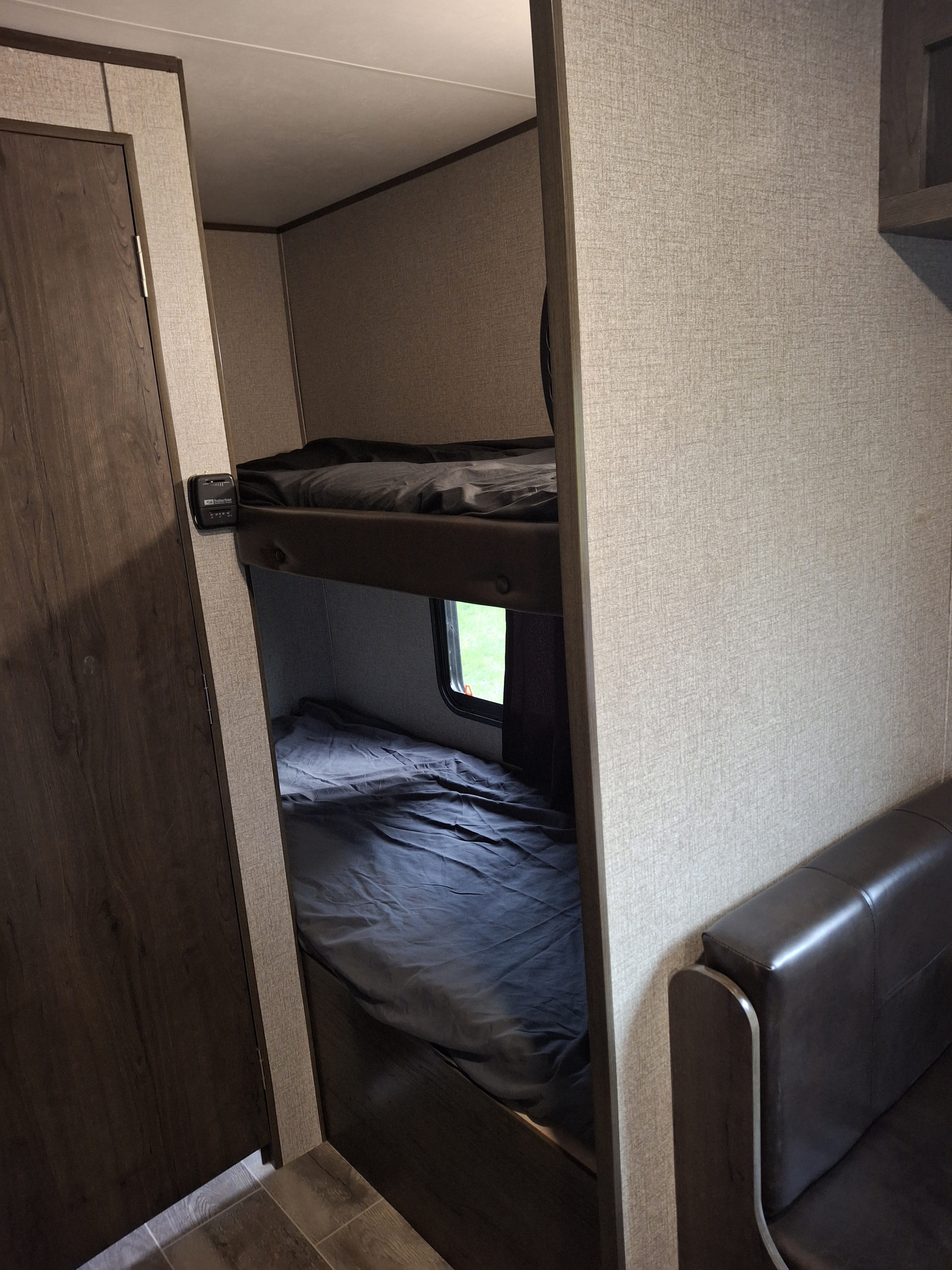 Interior view of an RV rental showing stacked bunk beds with dark bedding, a small window, and a brown bench seat.. Jayco Jay Feather 2022