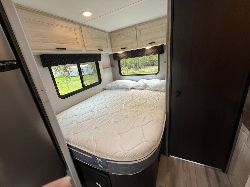 Cozy RV rental bedroom features a comfortable bed, overhead storage cabinets, and scenic window views for your trip.. Forest River Forester 2023
