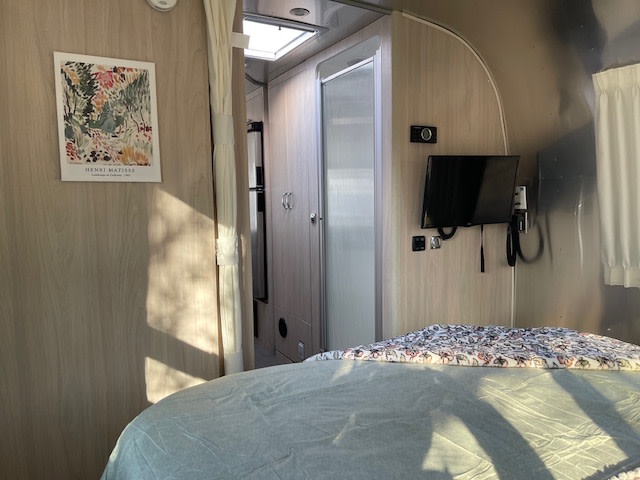 Inside a bright RV rental: features a comfortable bed, TV, and a Henri Matisse print, offering cozy travel comfort.. Airstream Globetrotter 2021