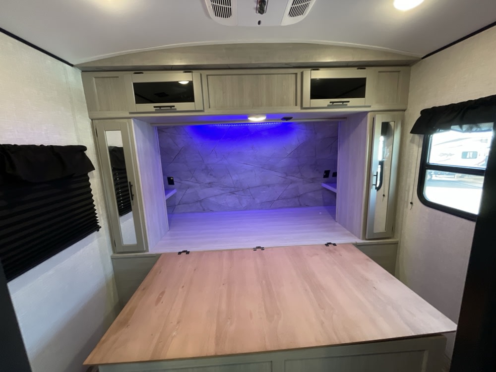 RV rental interior: a modern bedroom with a convertible fold-out bed, overhead storage, and blue accent lighting, designed for compact living.. Crossroads RV Sunset Trail Super Lite 2023