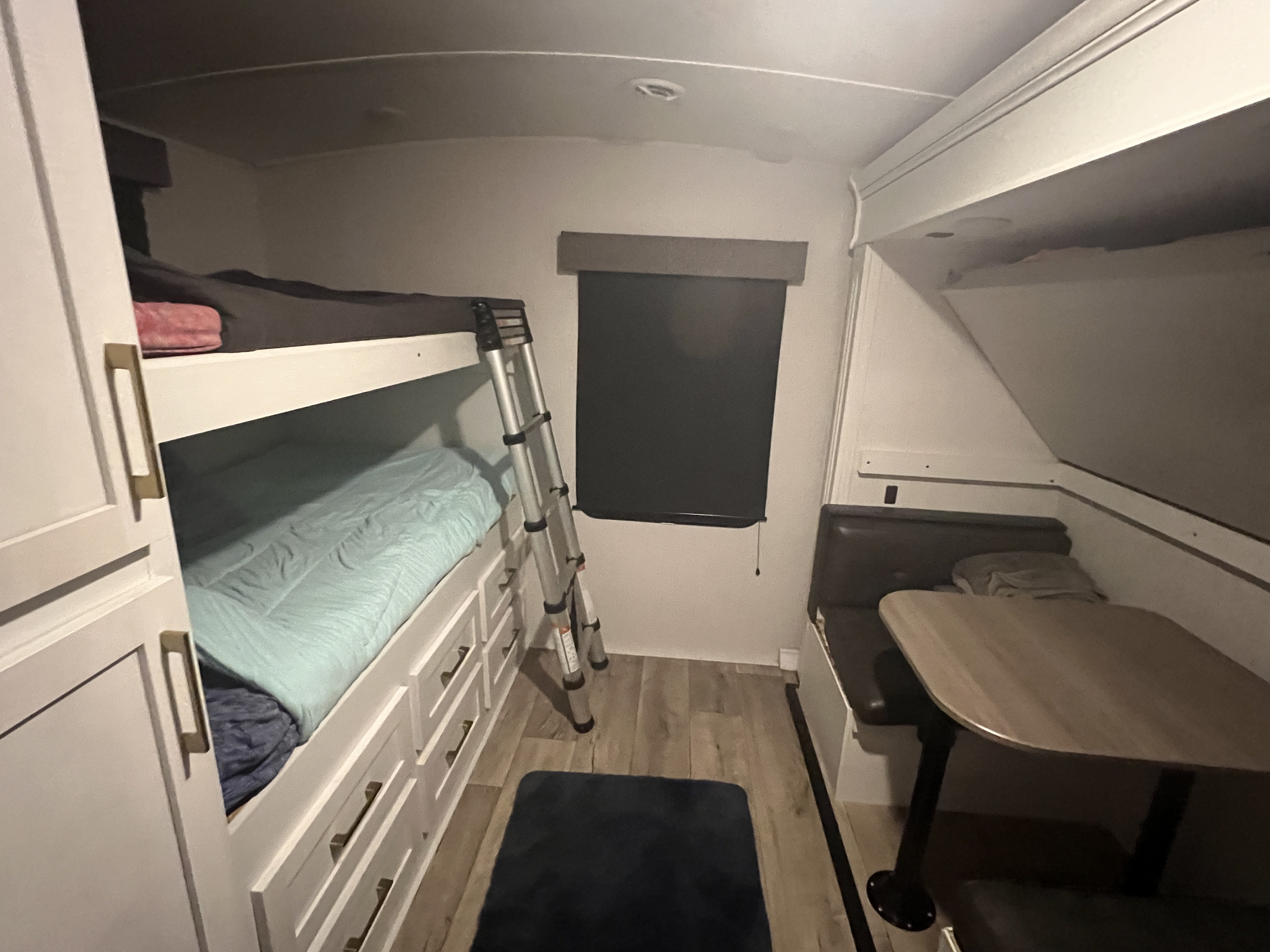 Cozy RV rental interior featuring bunk beds with storage drawers, a ladder, and a dinette booth with table.. Astoria Astoria Trailer 2022