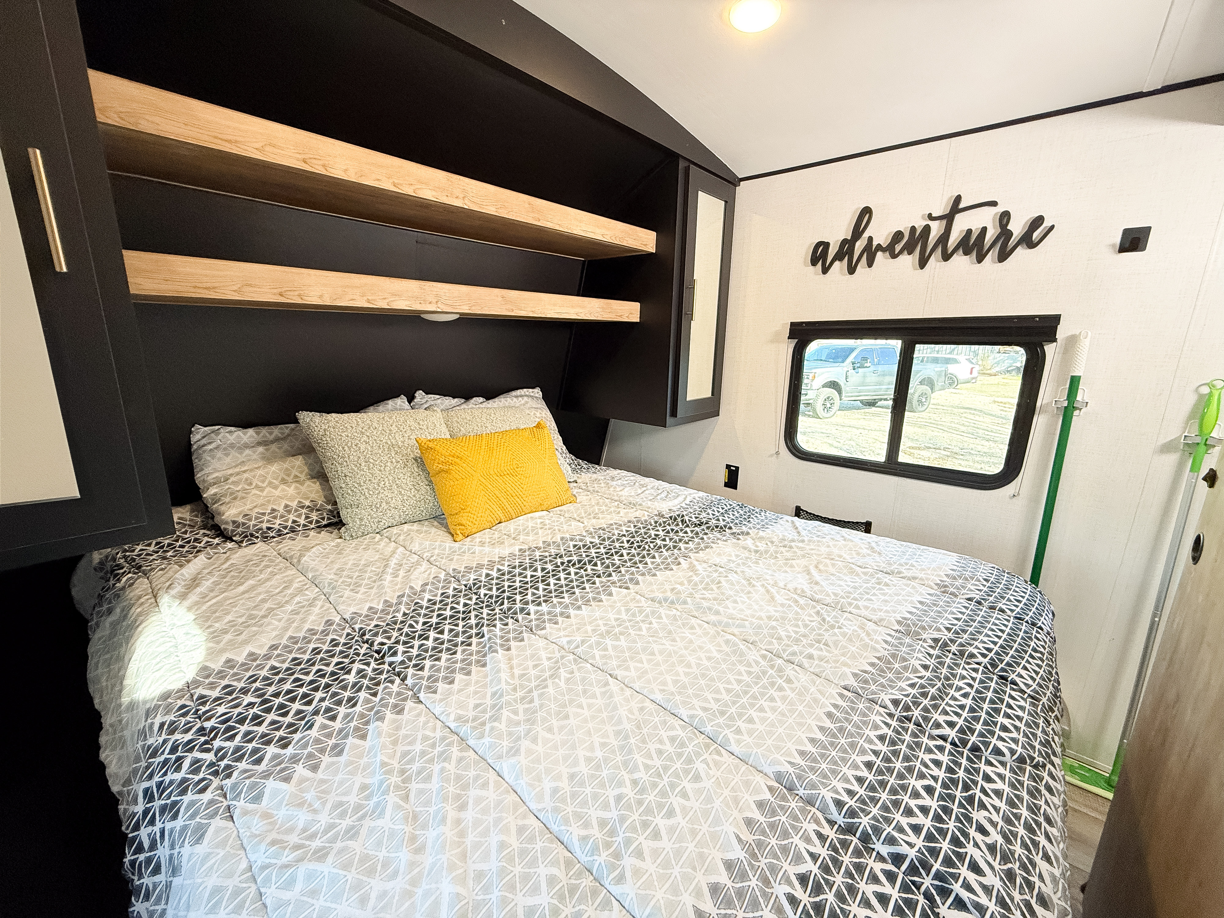 Comfortable RV rental sleeping area with black and wood shelving, a large bed with patterned bedding, and 'adventure' decor.. Keystone Springdale 2024