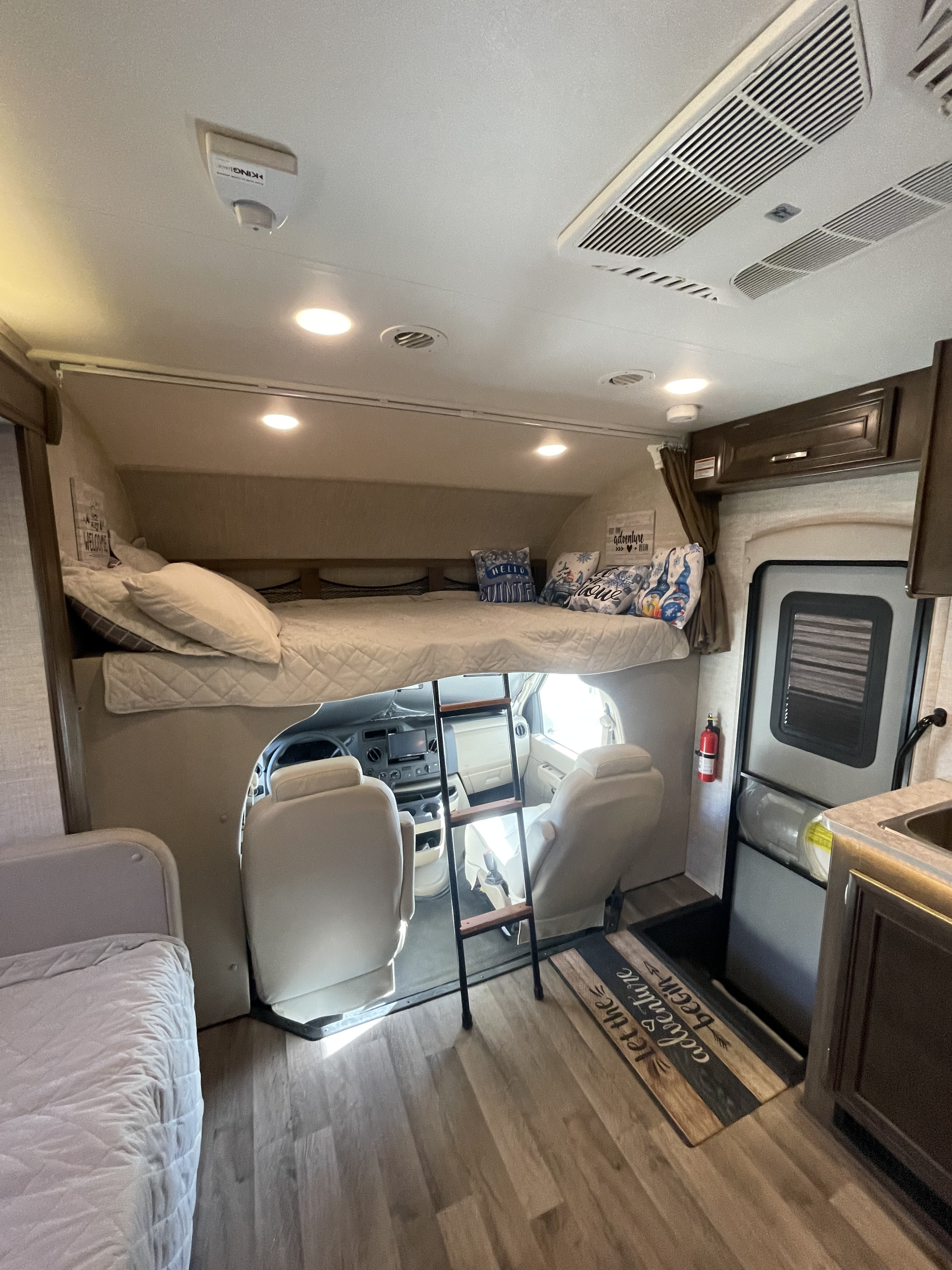 Spacious RV rental interior featuring a large overhead bunk bed, ladder, and driver's area below. Ideal for family adventures.. Jayco Redhawk 2021