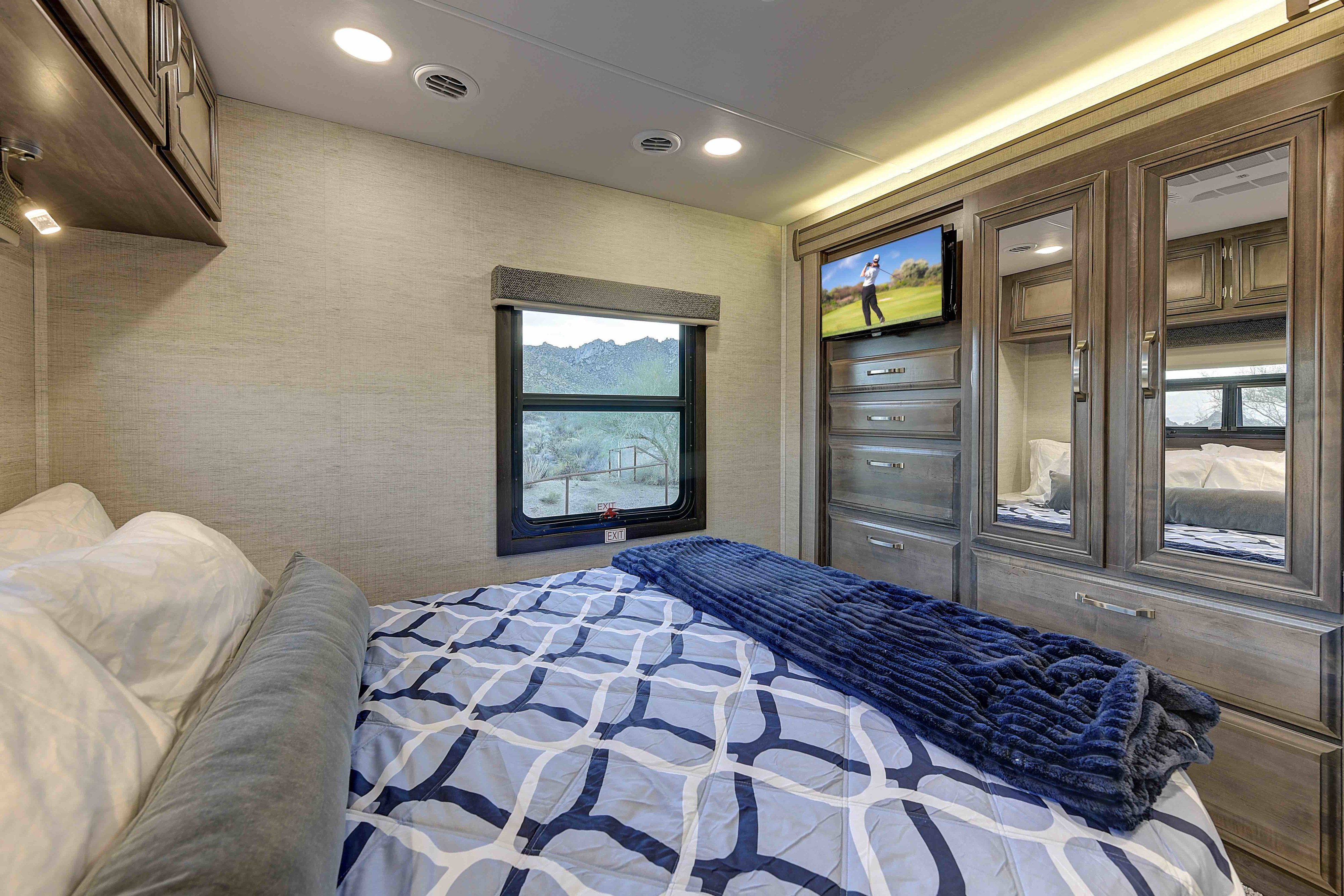 Cozy RV rental bedroom features a comfy bed, mounted TV, and window with desert views. Ideal for a relaxing trip.. Entegra Coach Esteem 2023
