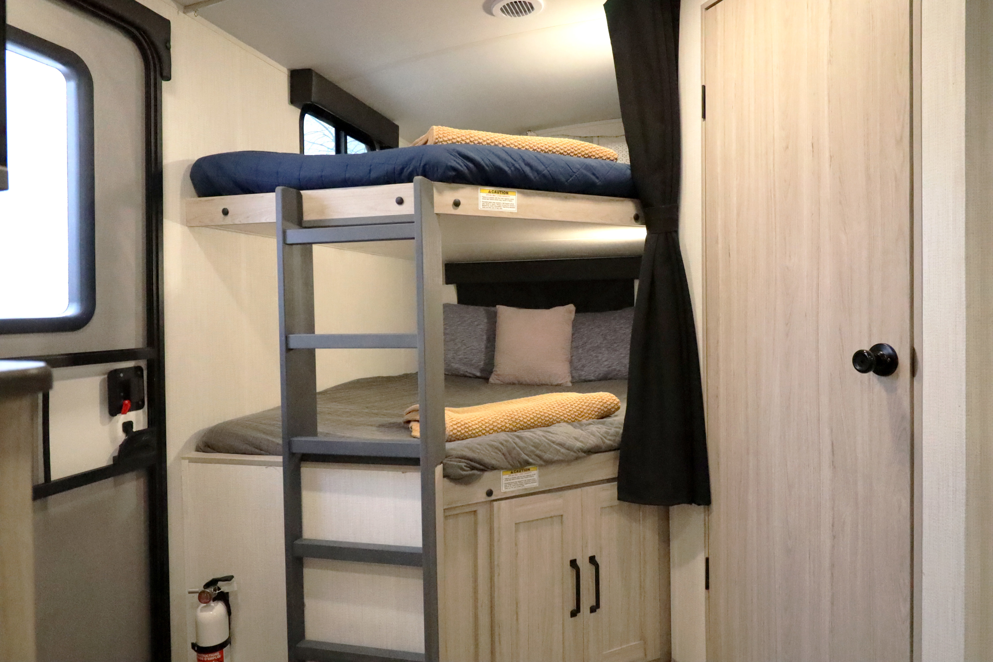 RV rental interior showcasing bunk beds with ladder, bedding, and storage. A fire extinguisher and ceiling vent are visible.. Heartland RVs Sundance Ultra Lite 2024