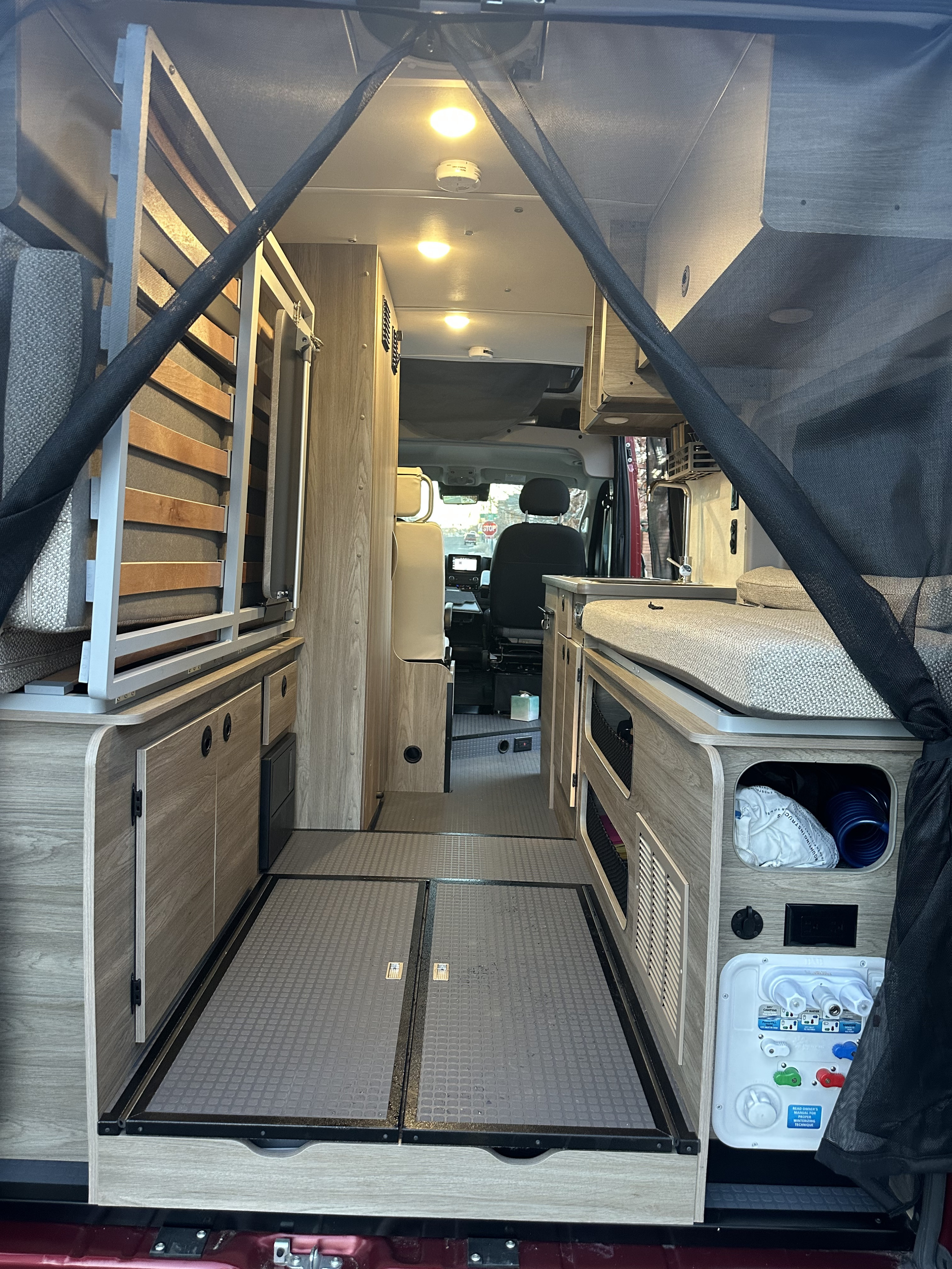 RV rental interior: A spacious van conversion with a convertible bed, storage, and water utility panel leading to the cockpit.. Winnebago Solis 2023