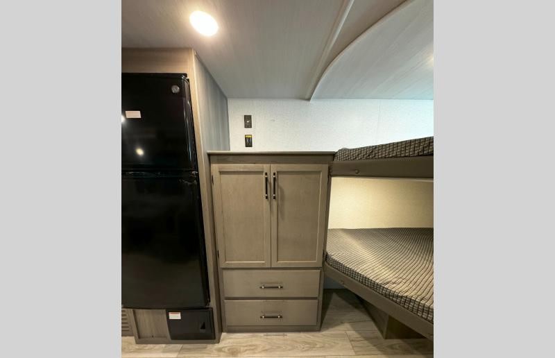 This RV rental interior features a black refrigerator, a wooden storage cabinet with drawers, and comfortable bunk beds.. Keystone Hideout 2025