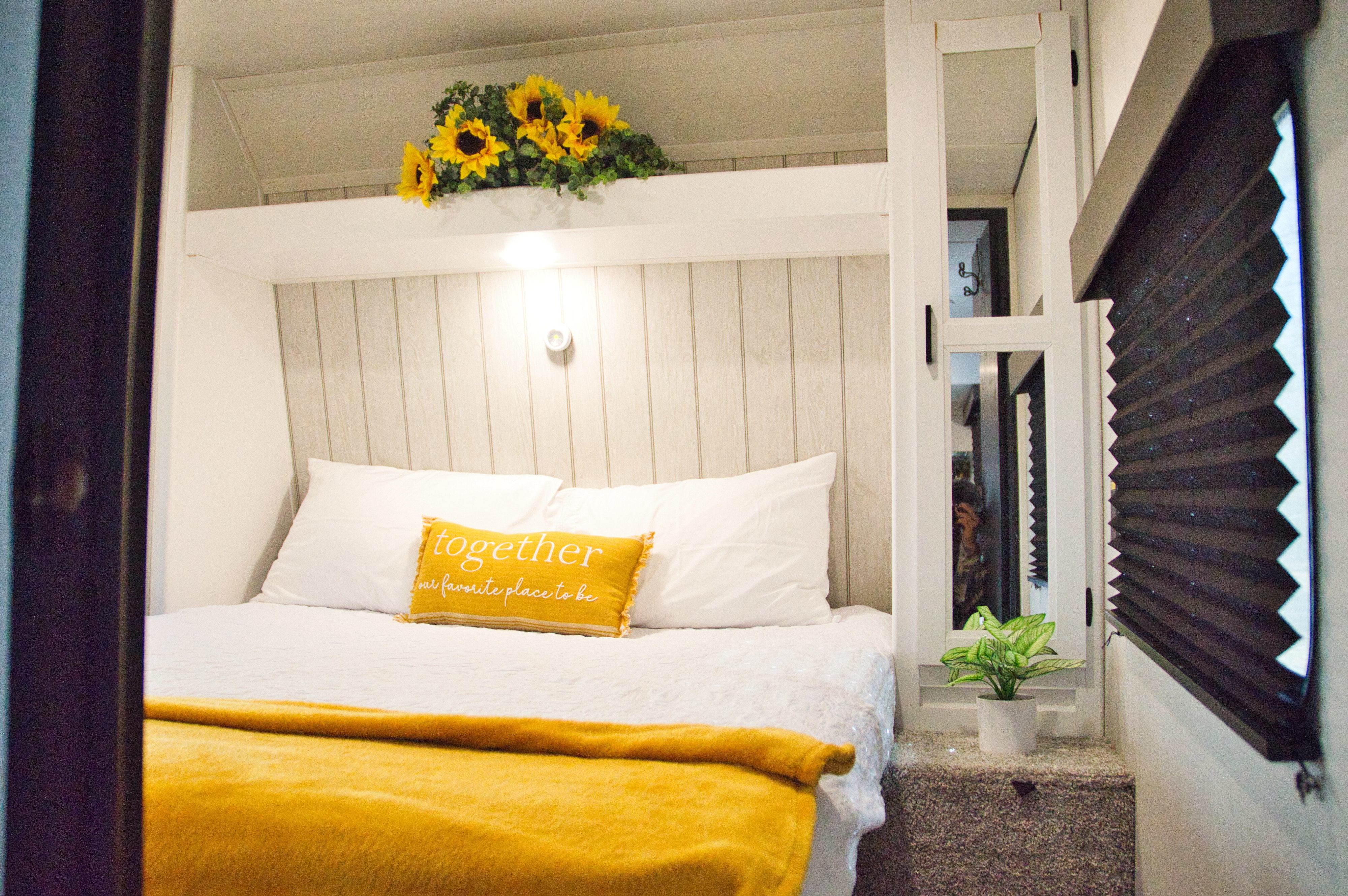 Cozy RV rental bedroom with white and yellow decor, featuring a comfortable bed and sunflower accents.. Keystone Hideout 2023