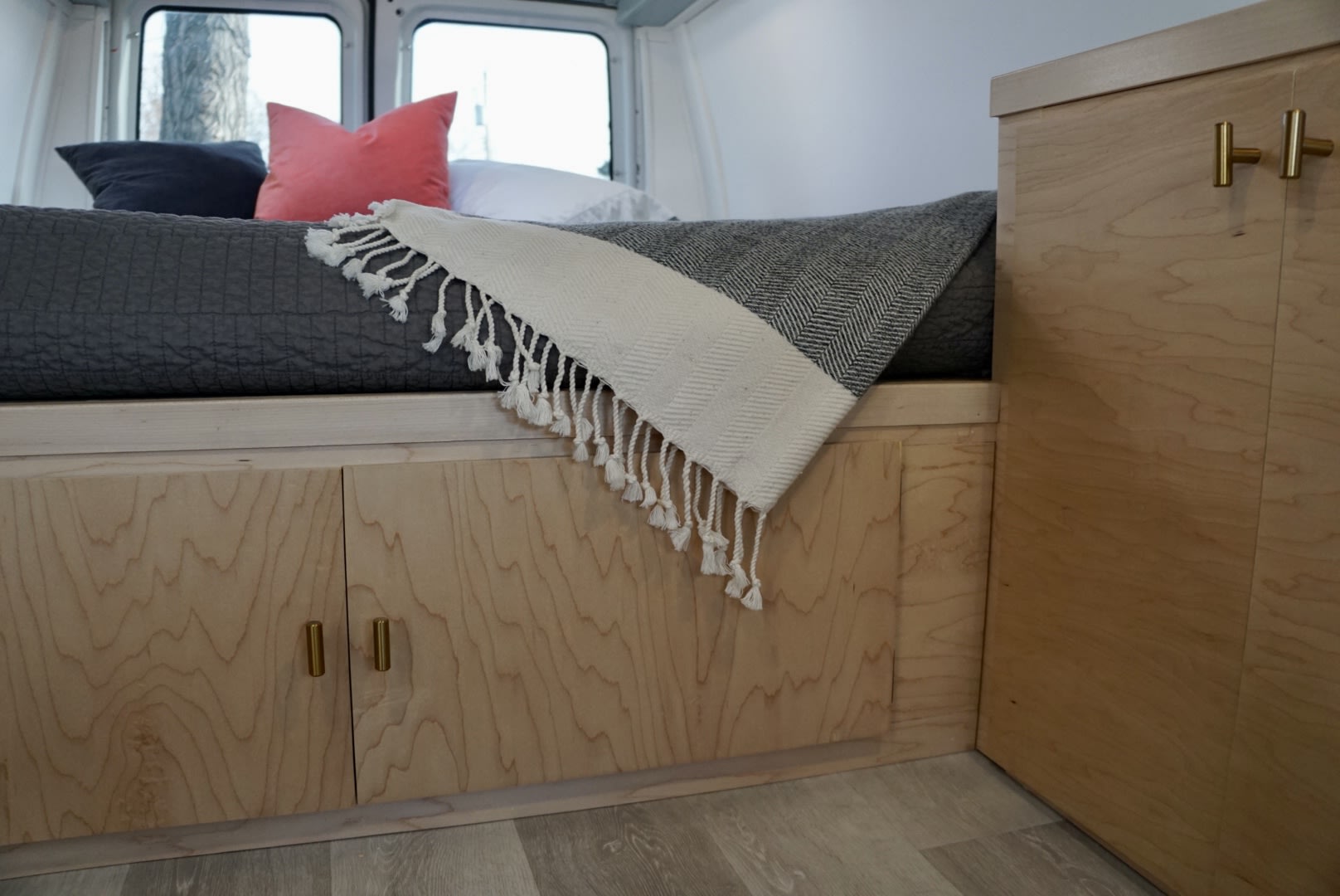 RV rental interior: cozy bed with grey duvet, patterned throw, and sleek wooden under-bed storage with brass handles.. Ford Econoline 150 2011