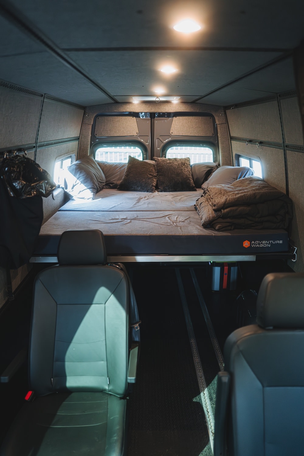 Adventure Wagon RV rental: cozy camper van interior with a comfortable bed, overhead lights, and passenger seating.. Mercedes-Benz Sprinter 2022