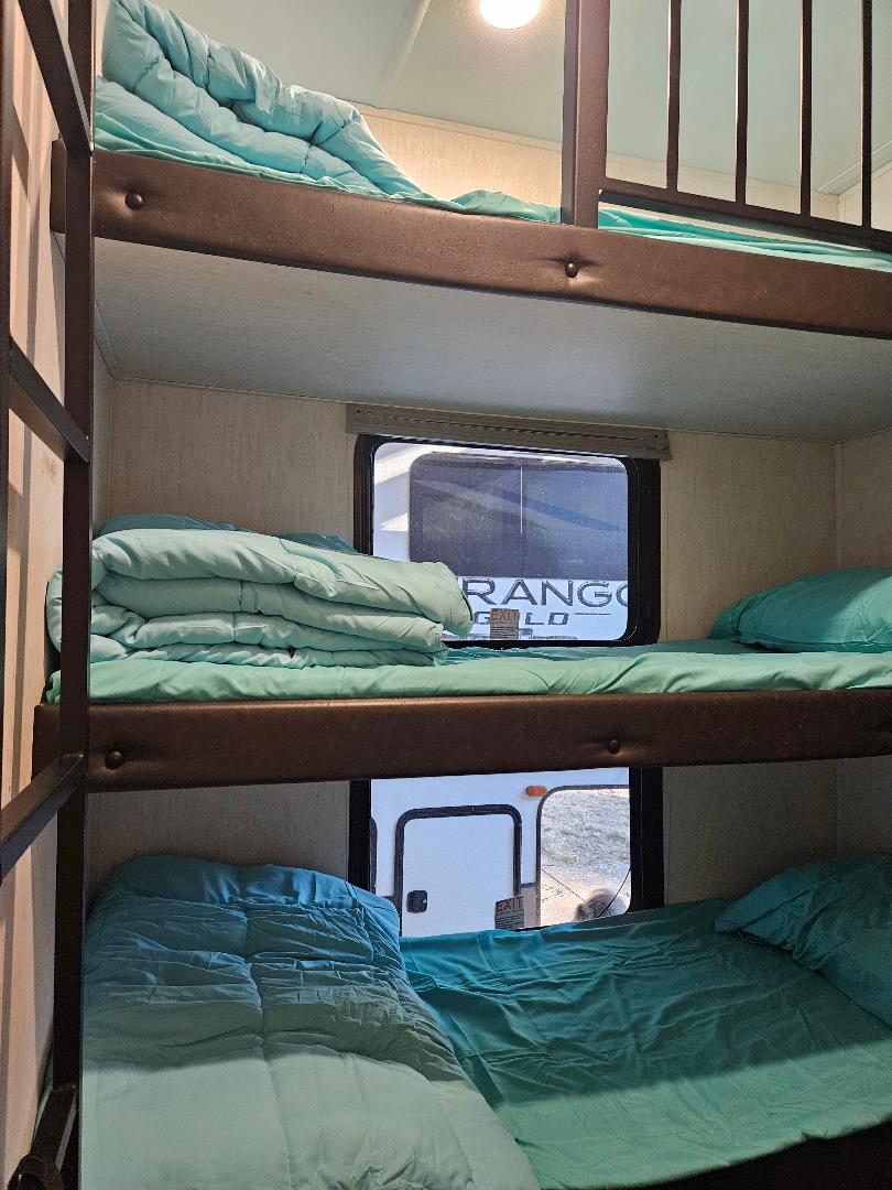 Inside an RV rental, stacked bunk beds with bright turquoise bedding provide comfortable sleeping. Windows show the outdoors.. Forest River Cherokee Arctic Wolf 2022