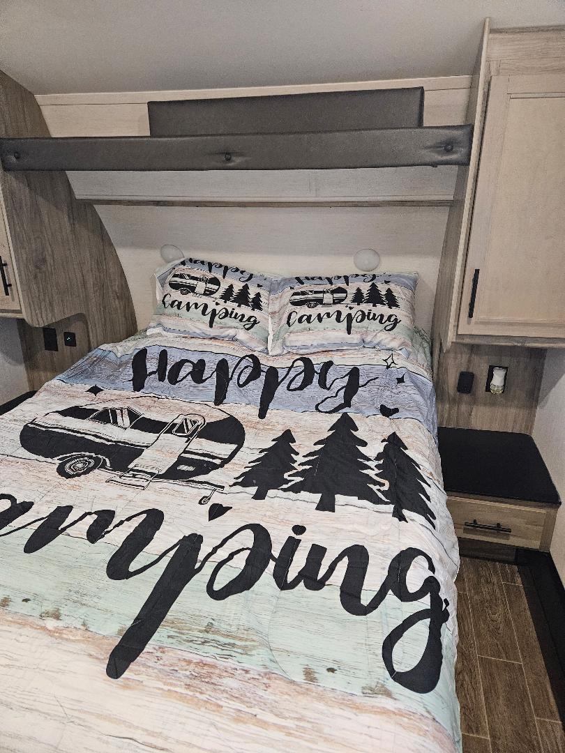Cozy RV rental bedroom with "Happy Camping" bedding and built-in storage, perfect for a comfortable adventure.. Forest River Cherokee Arctic Wolf 2022