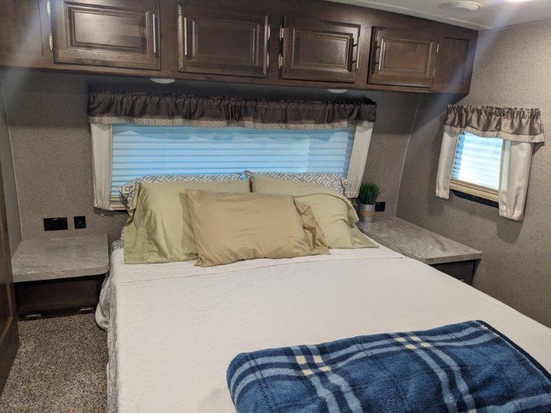 Experience comfort in this RV rental bedroom: cozy bed, overhead wood cabinets, and side tables. Perfect for your trip.. Forest River Flagstaff Super Lite 2020