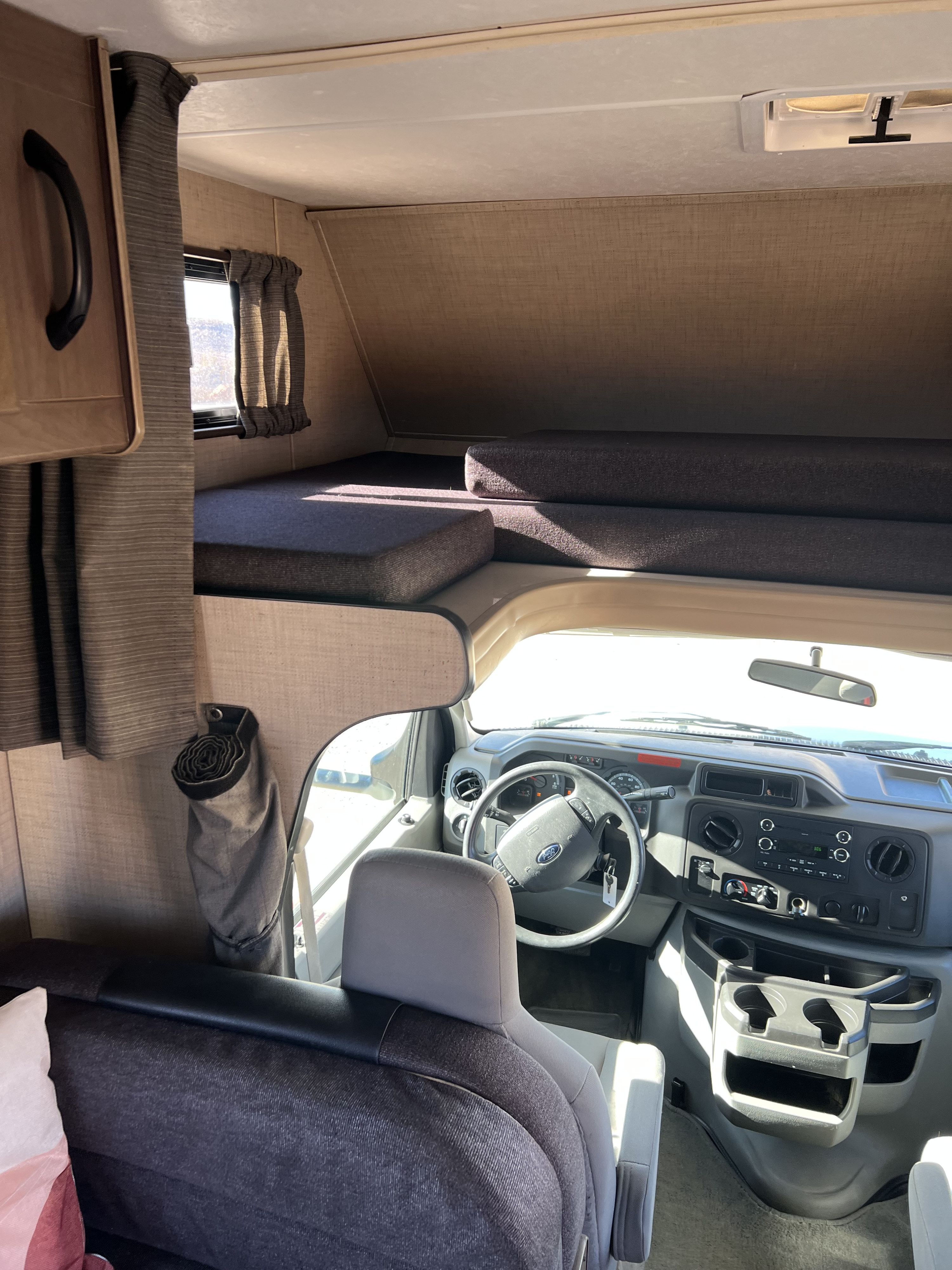 RV rental interior. Shows the comfortable cab-over bunk area with cushions, and the driver's cockpit with steering wheel and dashboard.. Thor Majestic 2018
