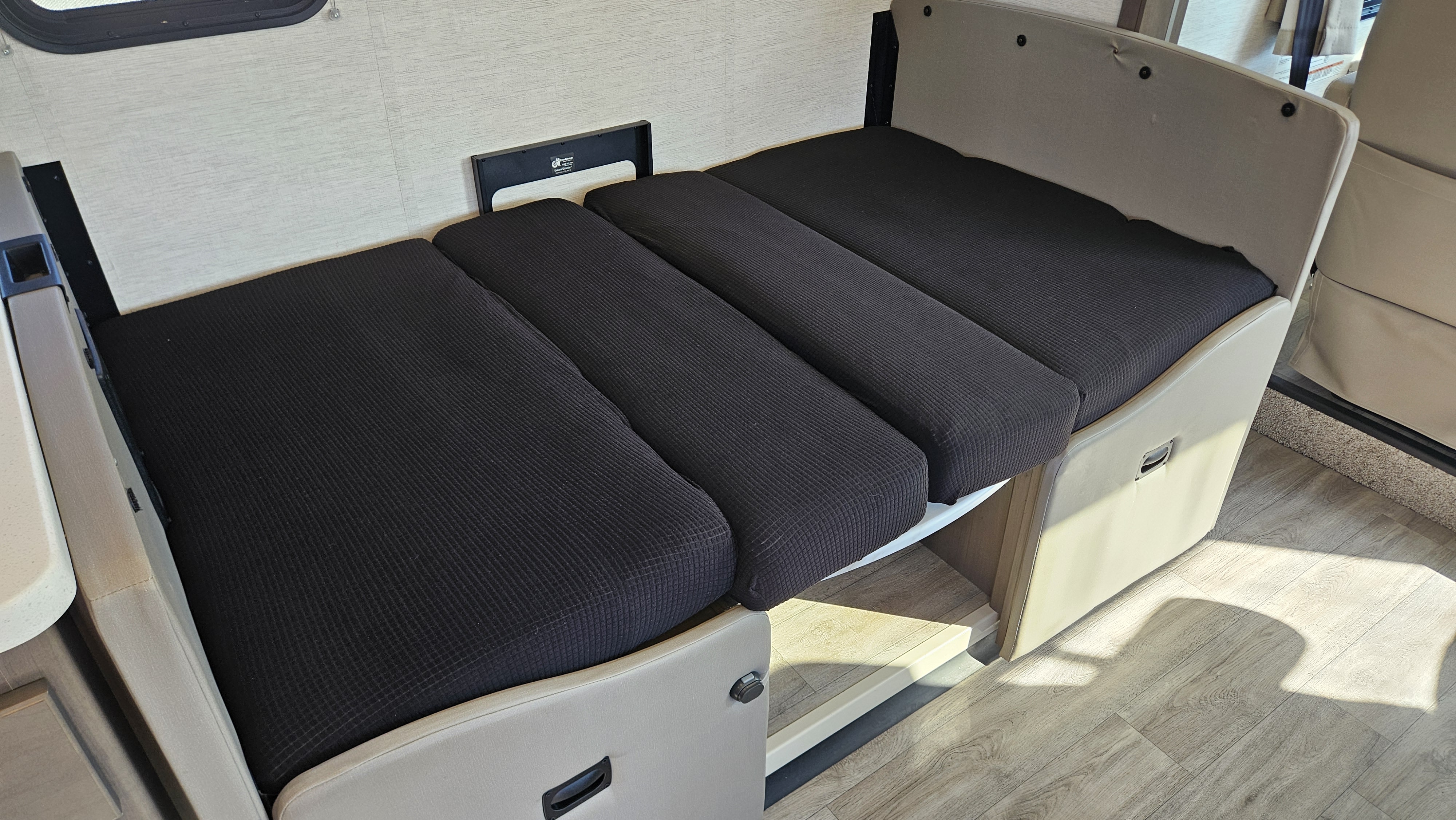 RV rental dinette converted into a comfortable bed with black cushions, perfect for maximizing interior space.. Thor ACE 2024