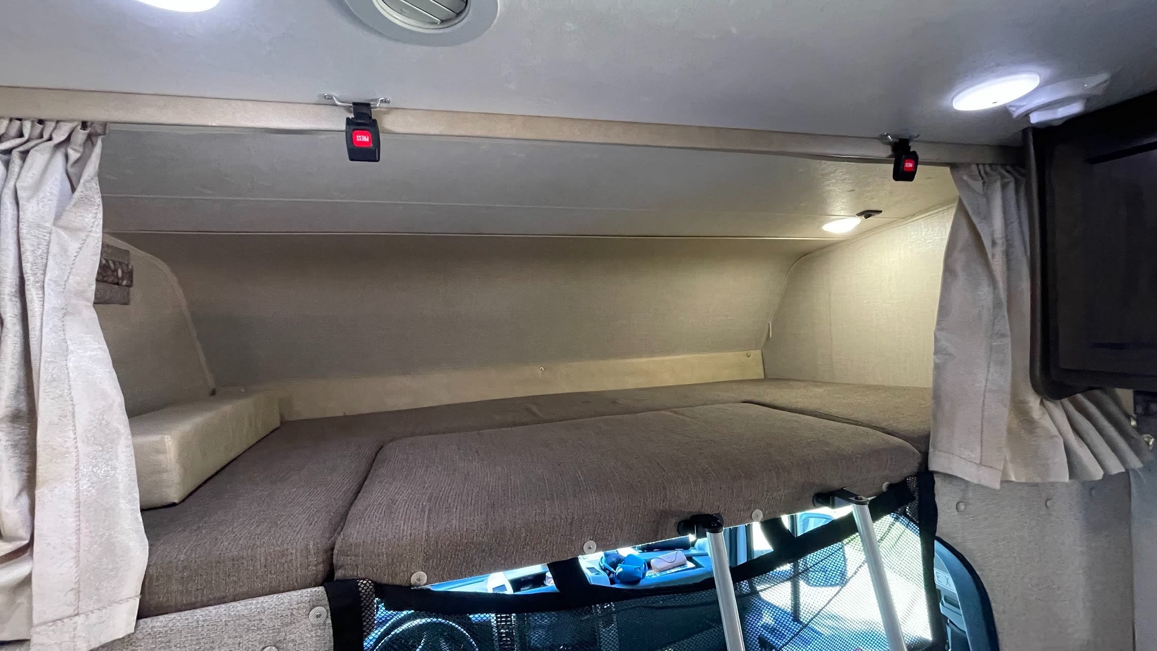 This RV rental features a cozy over-cab bunk bed, complete with mattress, curtains, and overhead lights for a comfortable sleeping area.. Mercedes Coachmen Prism 2200FS 2020