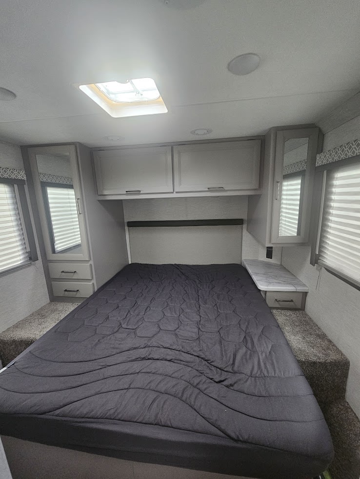 Spacious RV rental bedroom interior with large bed, overhead cabinets, and bright skylight for comfortable travel.. Thor Coleman 28AMC 2024