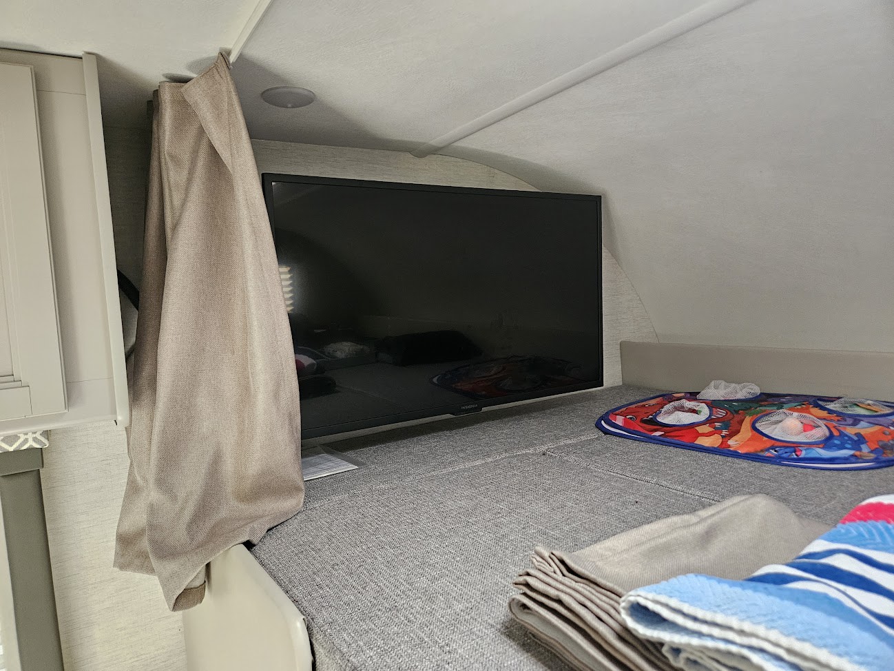 Inside an rv rental: a cozy sleeping area with a mounted TV, privacy curtain, and children's playmat on the bed.. Thor Coleman 28AMC 2024