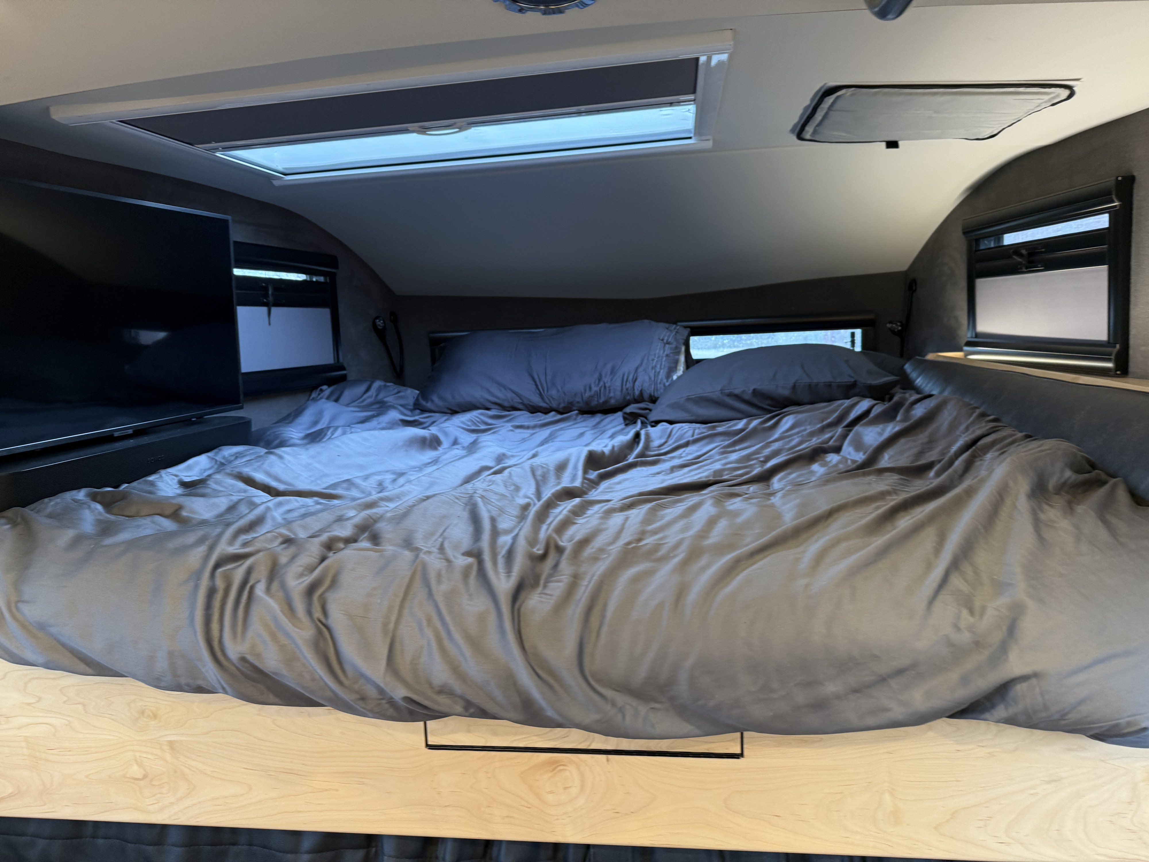 Cozy RV rental bedroom featuring a plush bed, TV, and skylights, perfect for a comfortable travel experience.. Earthroamer LTi 2022