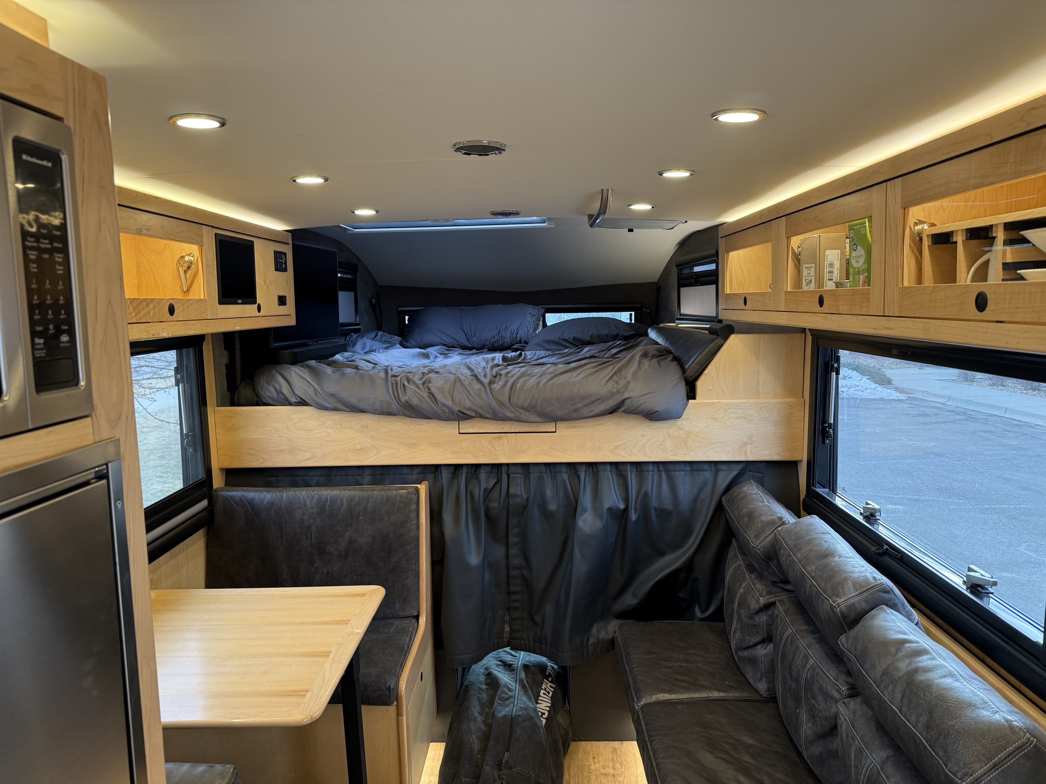 Bright RV rental interior: bed, dining booth, sofa, & kitchen. Wood cabinets and large windows inside this camper.. Earthroamer LTi 2022