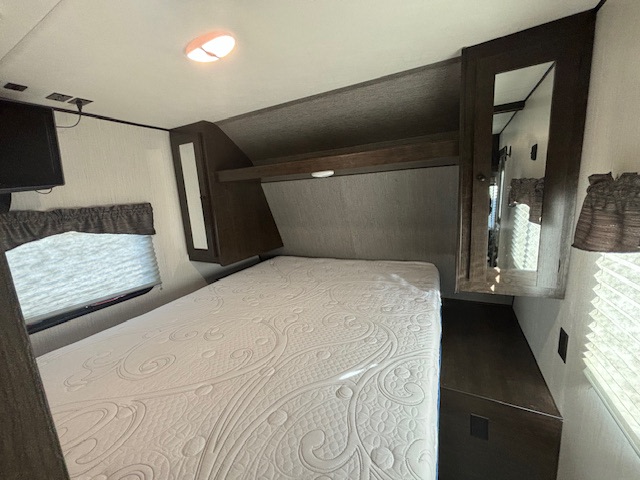 RV rental bedroom: bright interior with a comfy bed, overhead cabinets, TV, and windows. Your perfect travel retreat.. Prowler 262BHB 262BH 2020