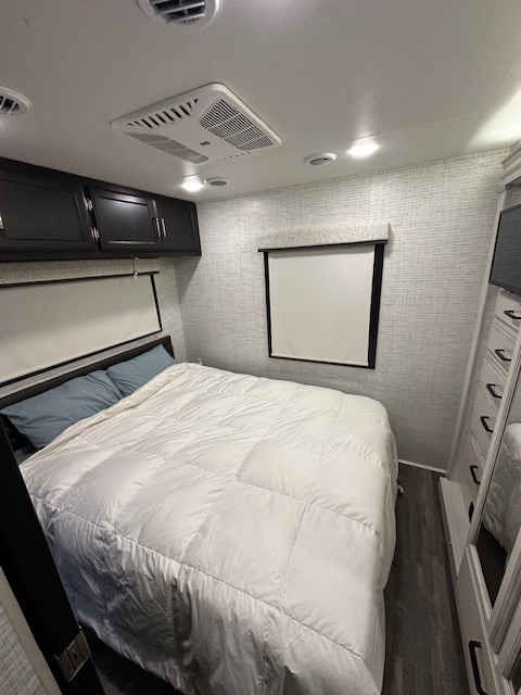 Modern RV rental bedroom with a spacious bed, overhead cabinets, AC unit, and bright recessed lighting. Ideal for comfortable travel.. Entegra Coach Vision 2024