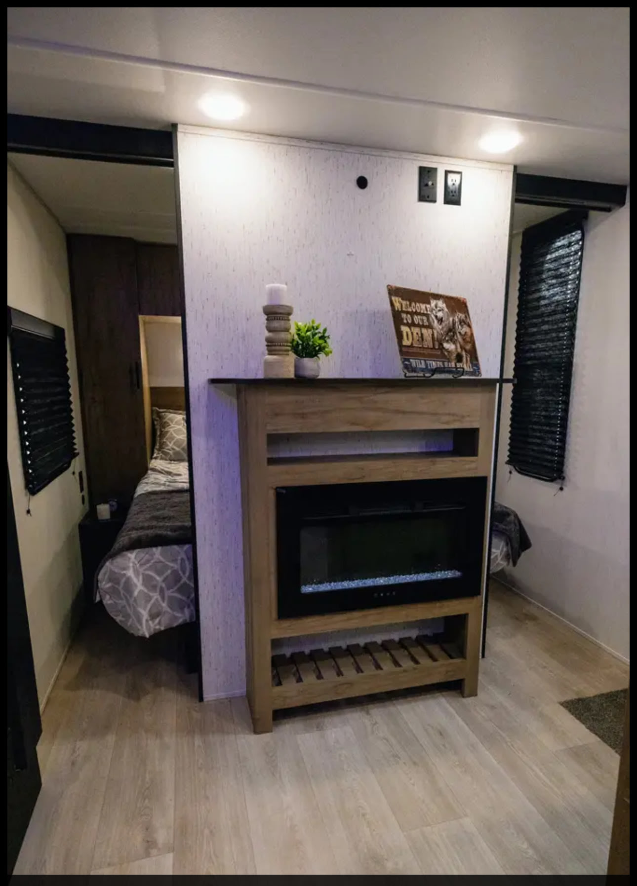 Compact RV rental interior featuring two separate sleeping areas, a central electric fireplace unit, and modern wood-look flooring.. Forest River 26DBH 2025