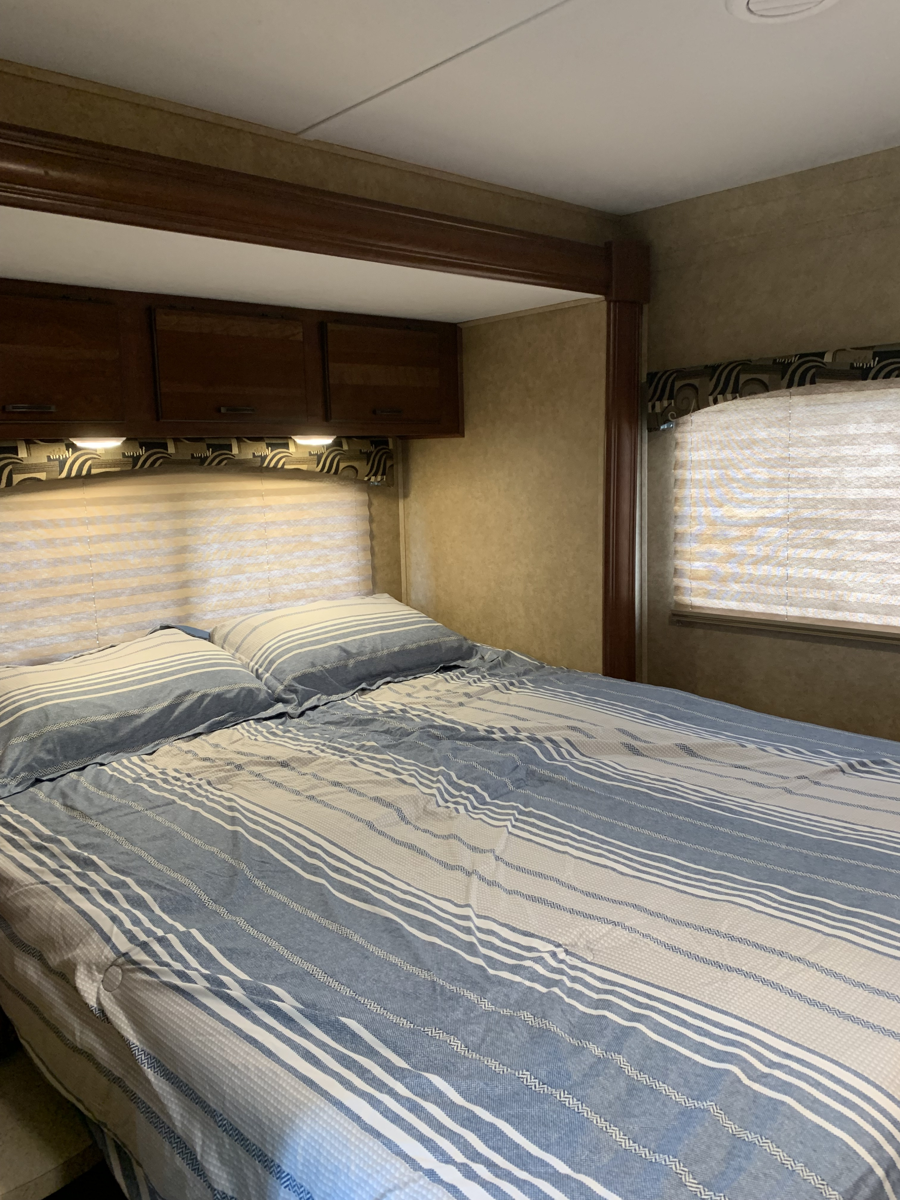 Cozy RV rental bedroom with striped bedding, overhead cabinets, and window blinds. A compact and inviting travel space.. Forest River Sunseeker 2014