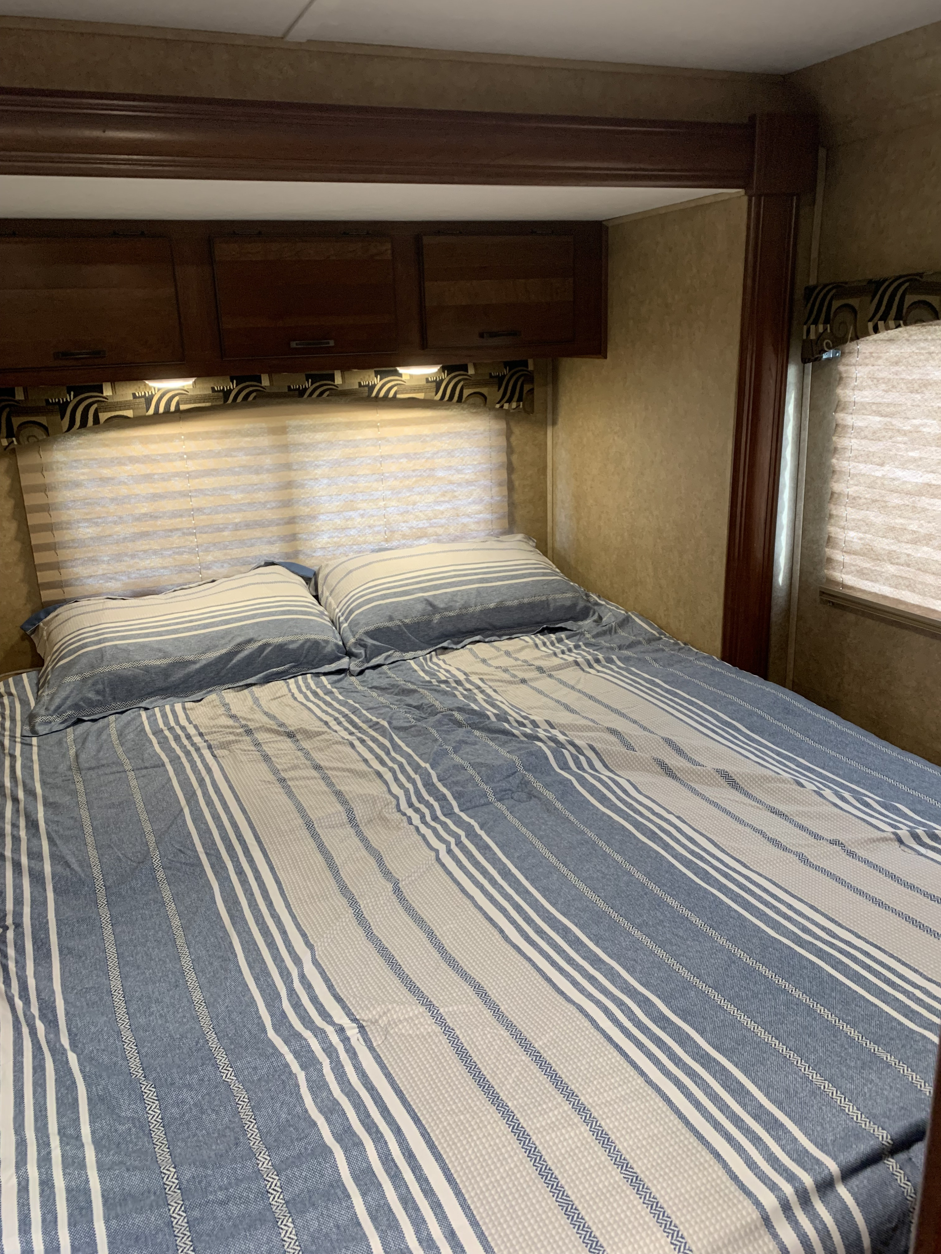 **RV rental** bedroom: a comfortable bed with blue and white striped bedding, overhead cabinets, and a window with blinds.. Forest River Sunseeker 2014