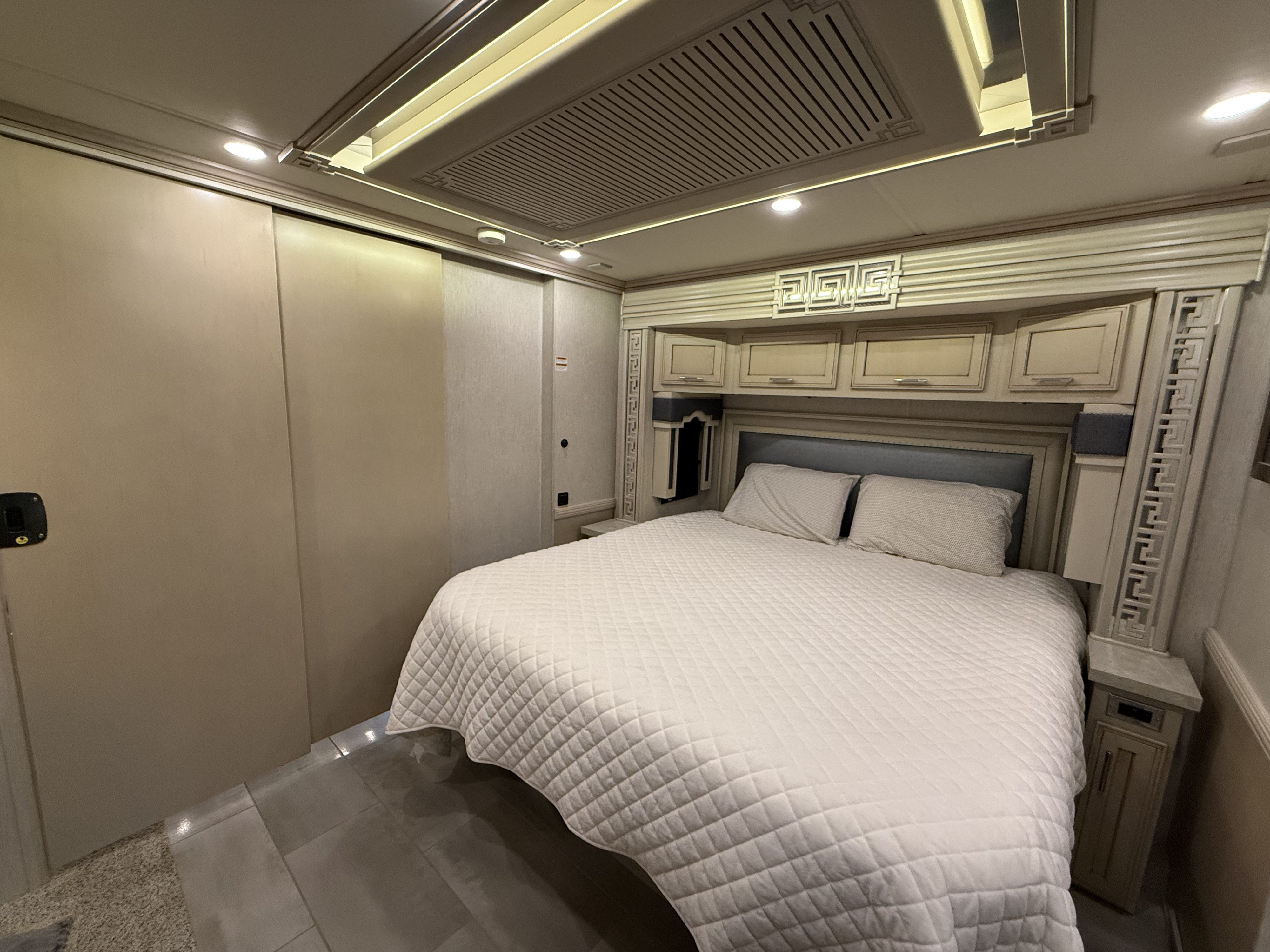 Explore this modern RV rental bedroom: large bed with quilted cover, ample overhead storage, and bright ambient lighting.. Newmar Ventana 2020