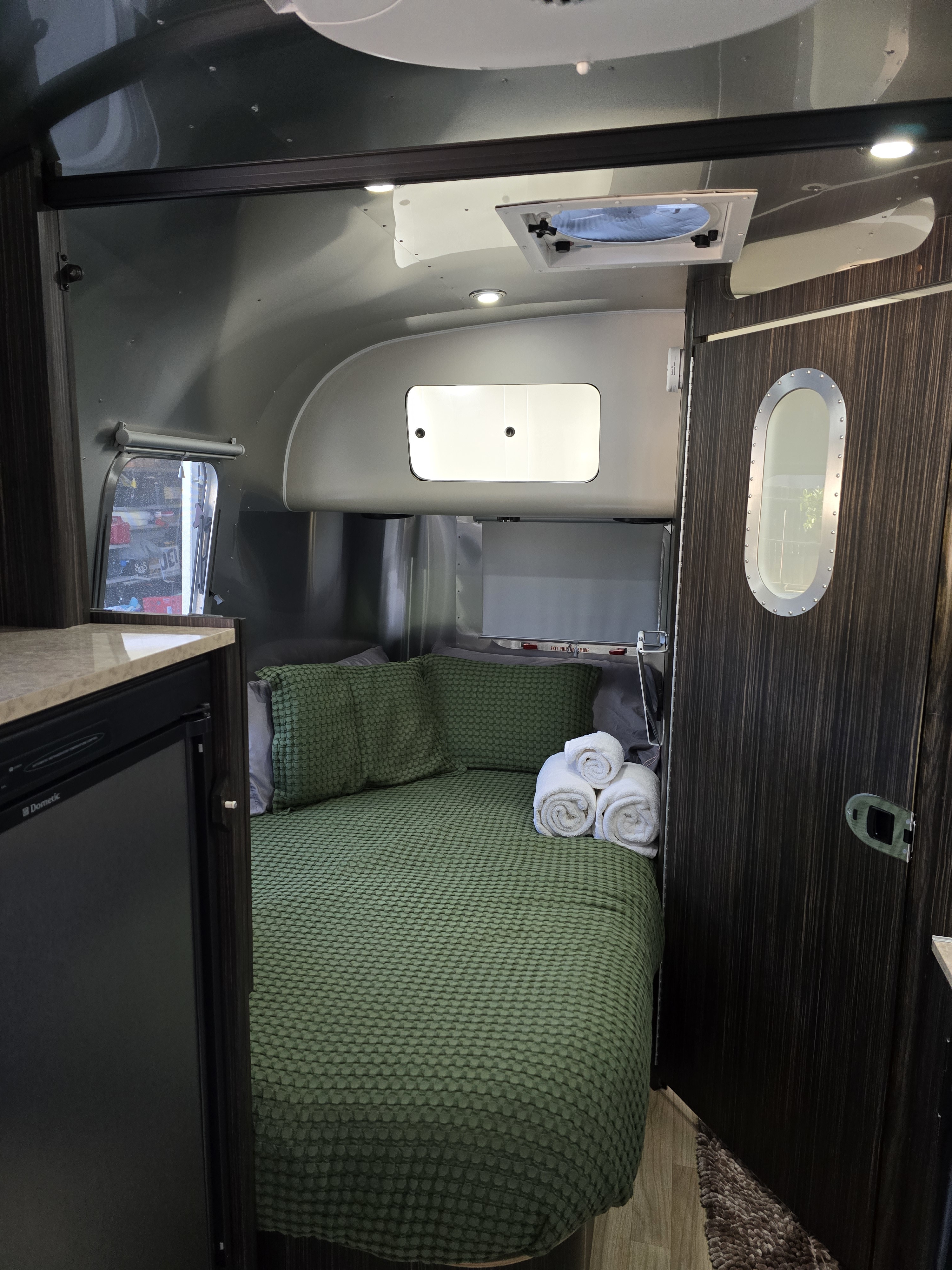 Cozy Airstream RV rental interior featuring a bed, kitchenette (fridge), and bright lighting. Ideal for travel.. Airstream International 2015