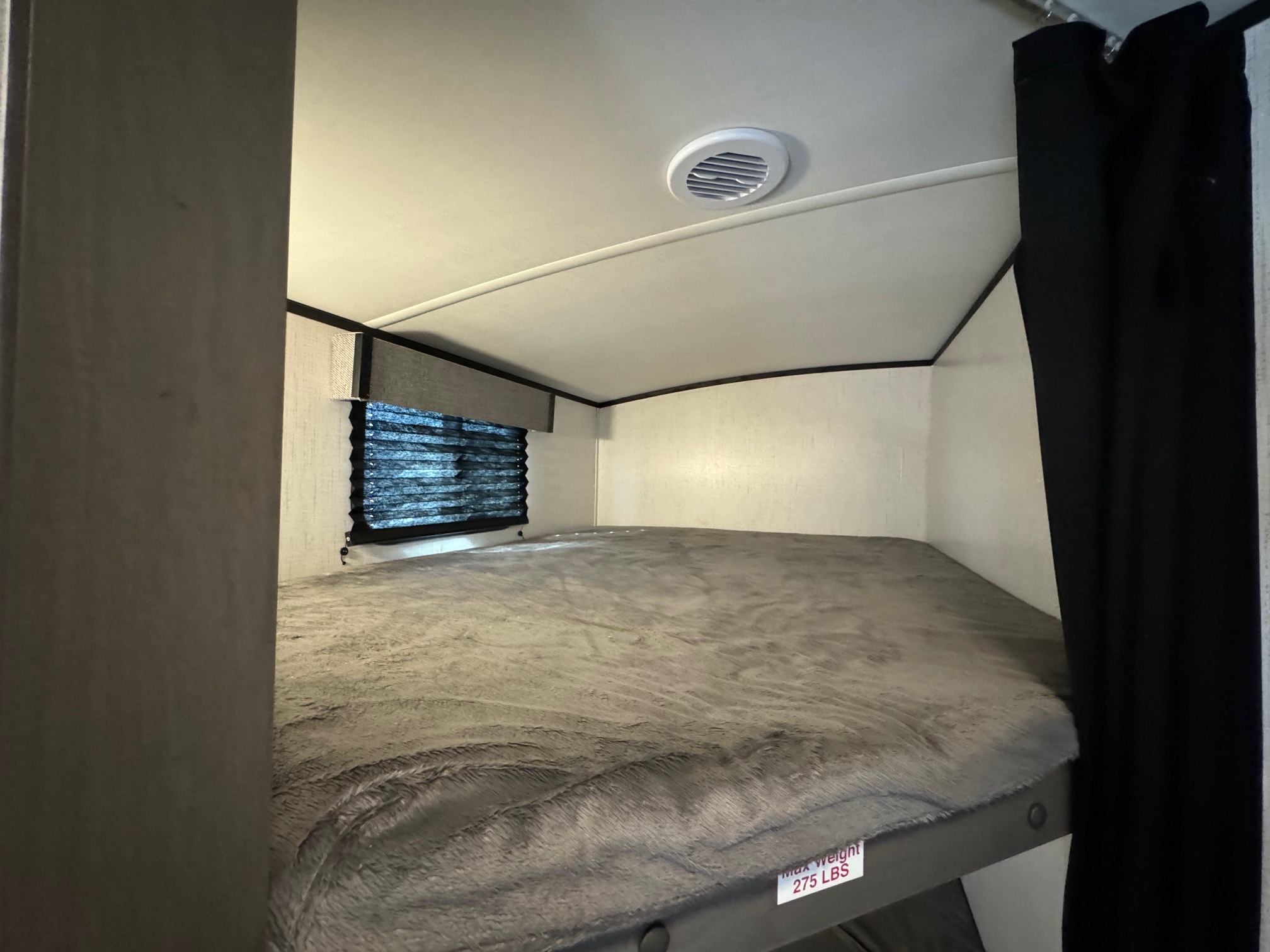 RV rental bunk bed with a soft grey blanket, window with blinds, and ceiling vent, showing a weight limit of 275 lbs.. Heartland Mpg 2022