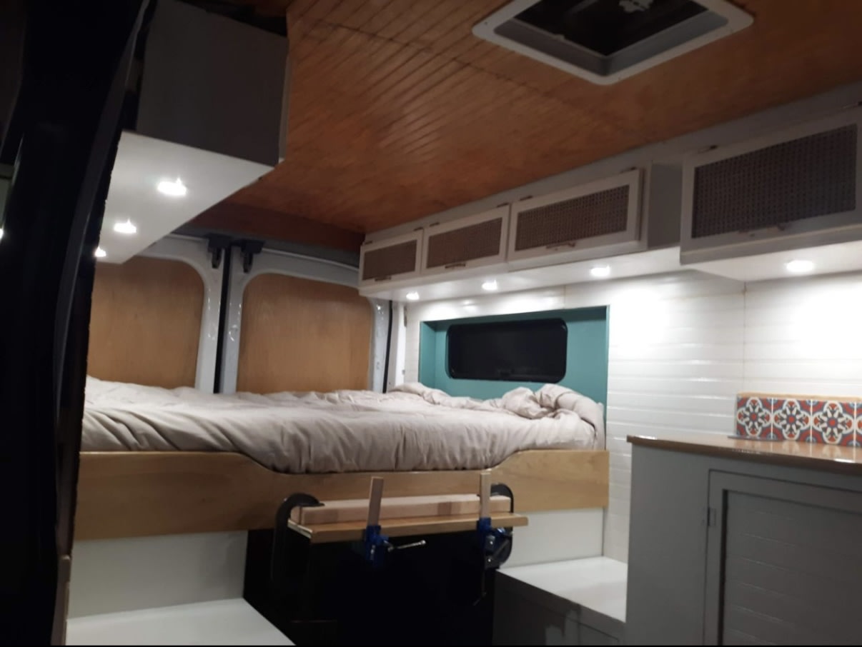 Inside this modern RV rental, a custom camper van conversion features a cozy bed, sleek cabinets, and bright lighting.. Ford Transit 2016
