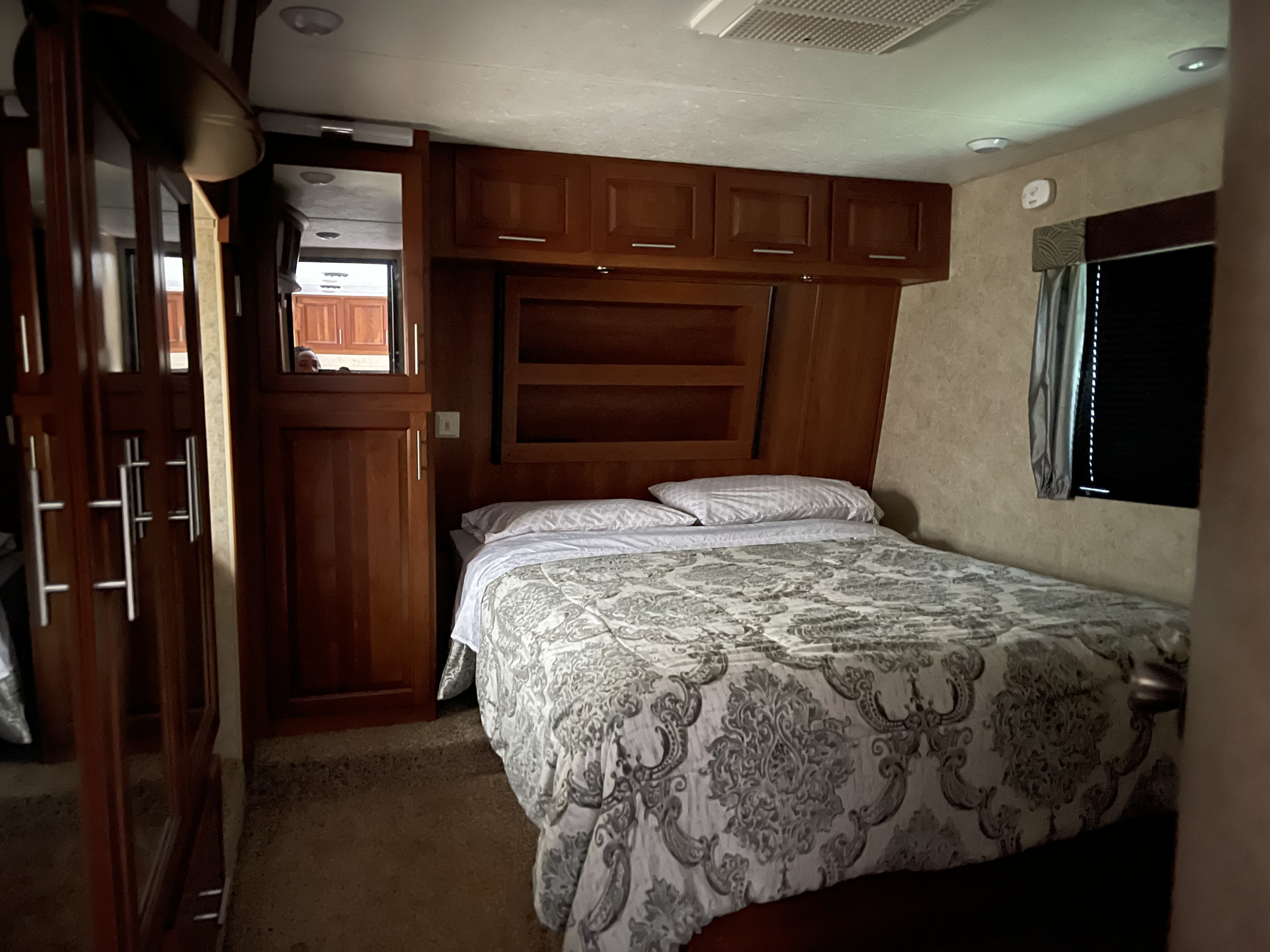 Comfortable RV rental bedroom showing a bed, overhead cabinets, a mirrored wardrobe, and a window.. Keystone Fuzion 2015
