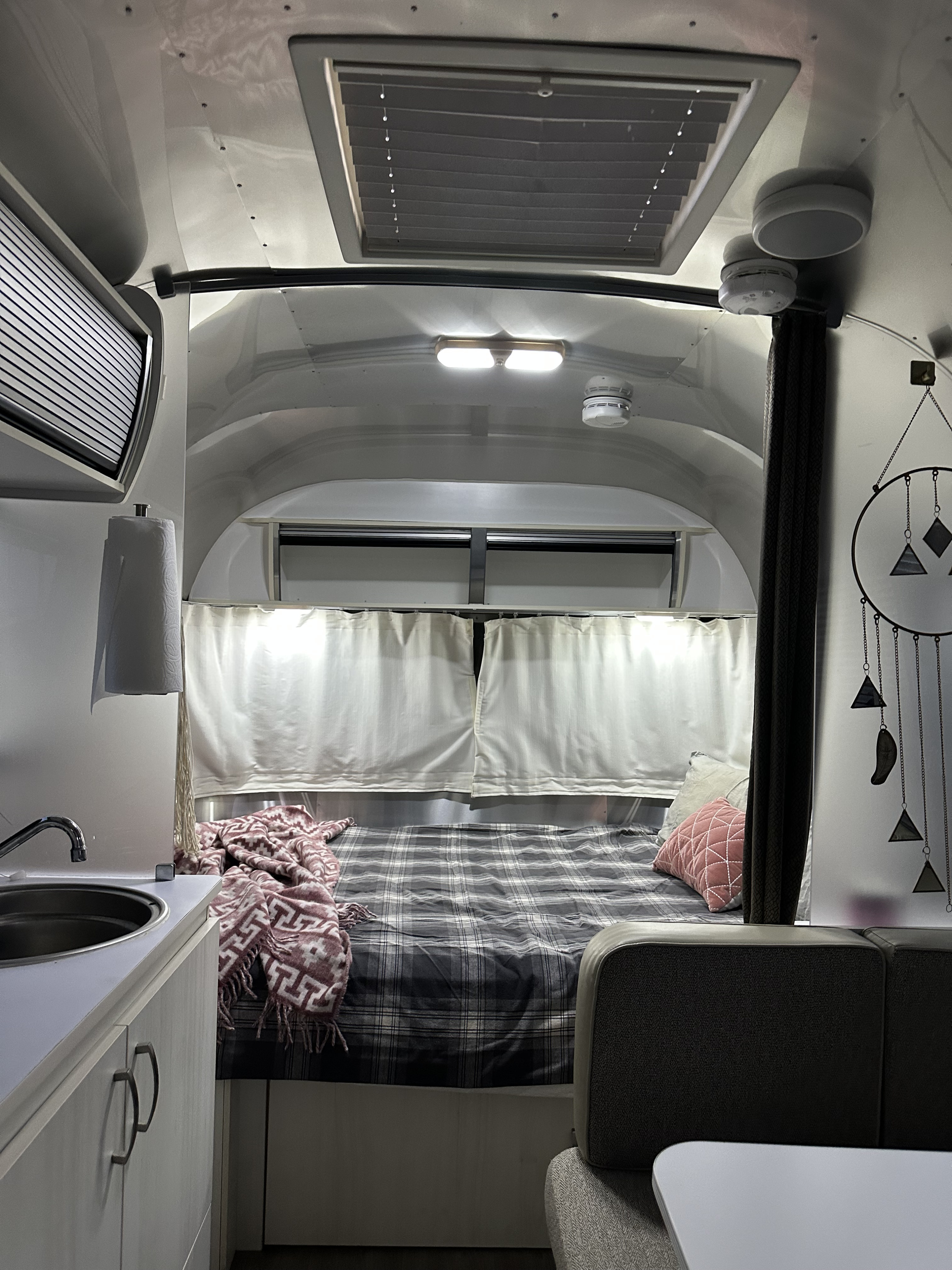 This RV rental offers a cozy interior with a plaid-covered bed, compact kitchenette, and a comfortable living space for travelers.. Airstream Sport 2016