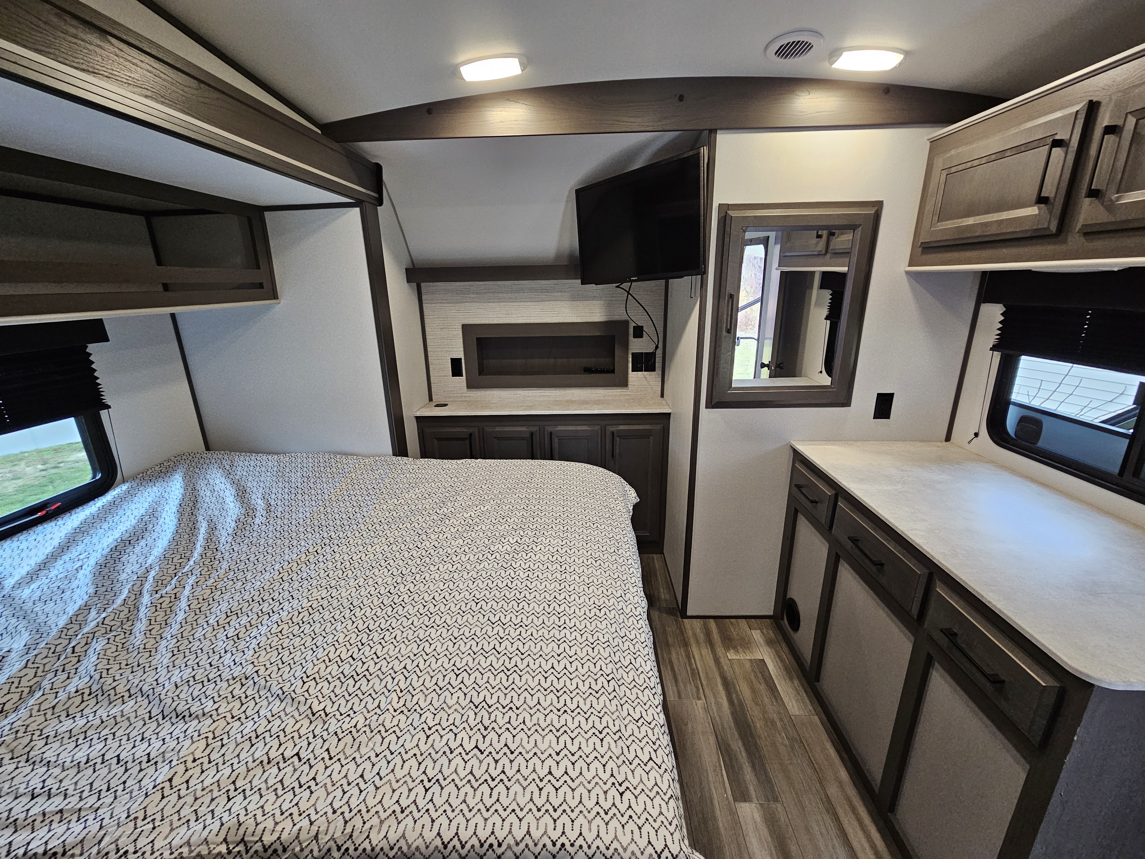 Cozy rv rental bedroom featuring a patterned bed, wall-mounted TV, storage cabinets, and wood-look flooring.. Heartland RVs Fuel Toy Hauler 2021