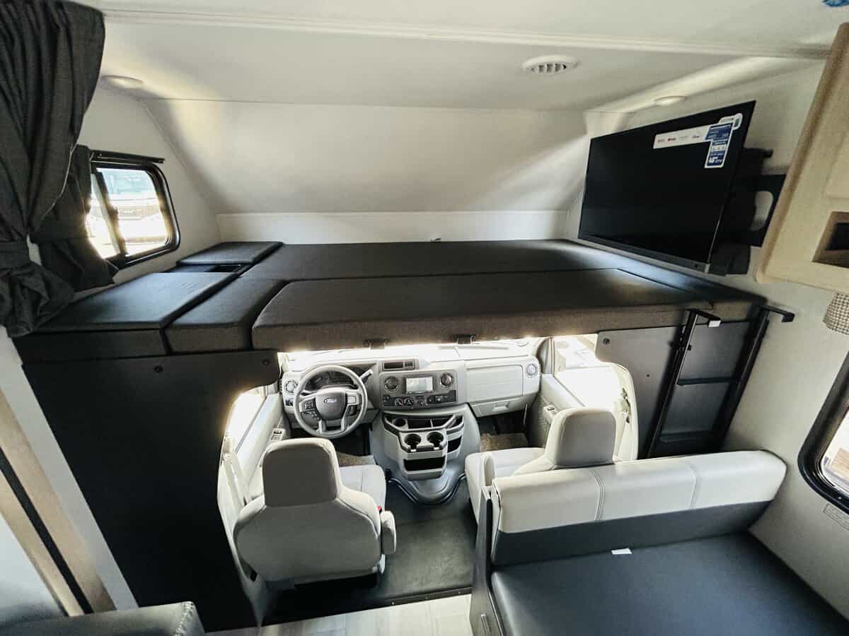Inside a modern RV rental, showing the driver's cab, large overhead bunk, TV, and rear dinette seating.. Forest River Sunseeker 2025