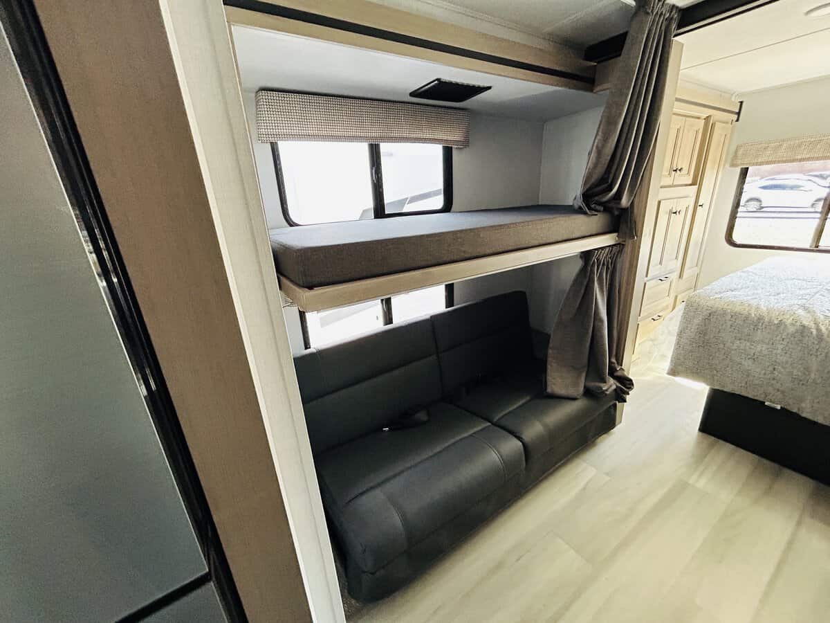 Spacious RV rental interior featuring comfortable bunk beds, a convertible sofa, and a main bed. Perfect for family adventures.. Forest River Sunseeker 2025