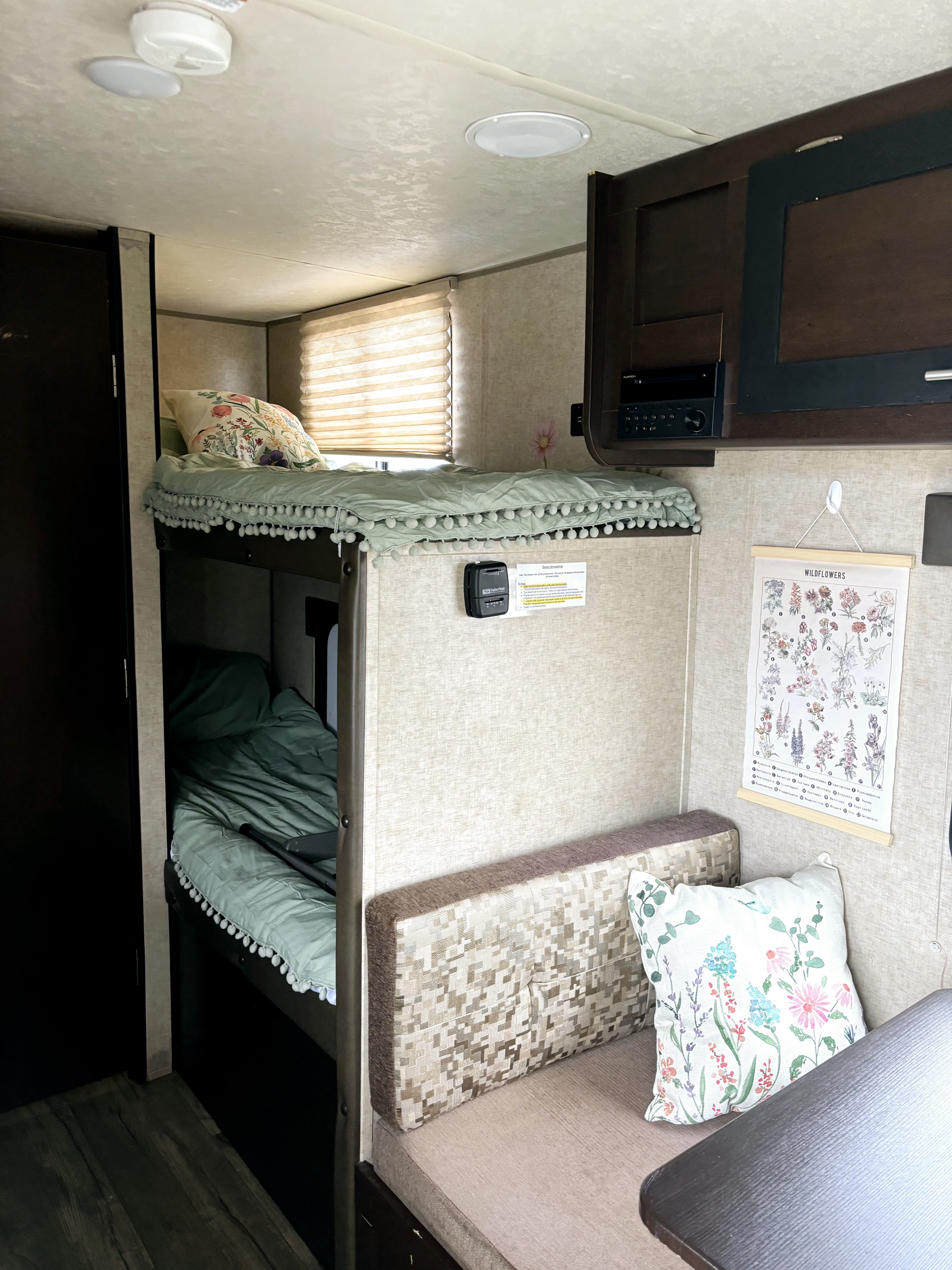 Inside a cozy RV rental: bunk beds with pom-pom bedding, a seating area with floral accents, and a "Wildflowers" chart.. Forest River Cherokee Wolf Pup Cascade 2017