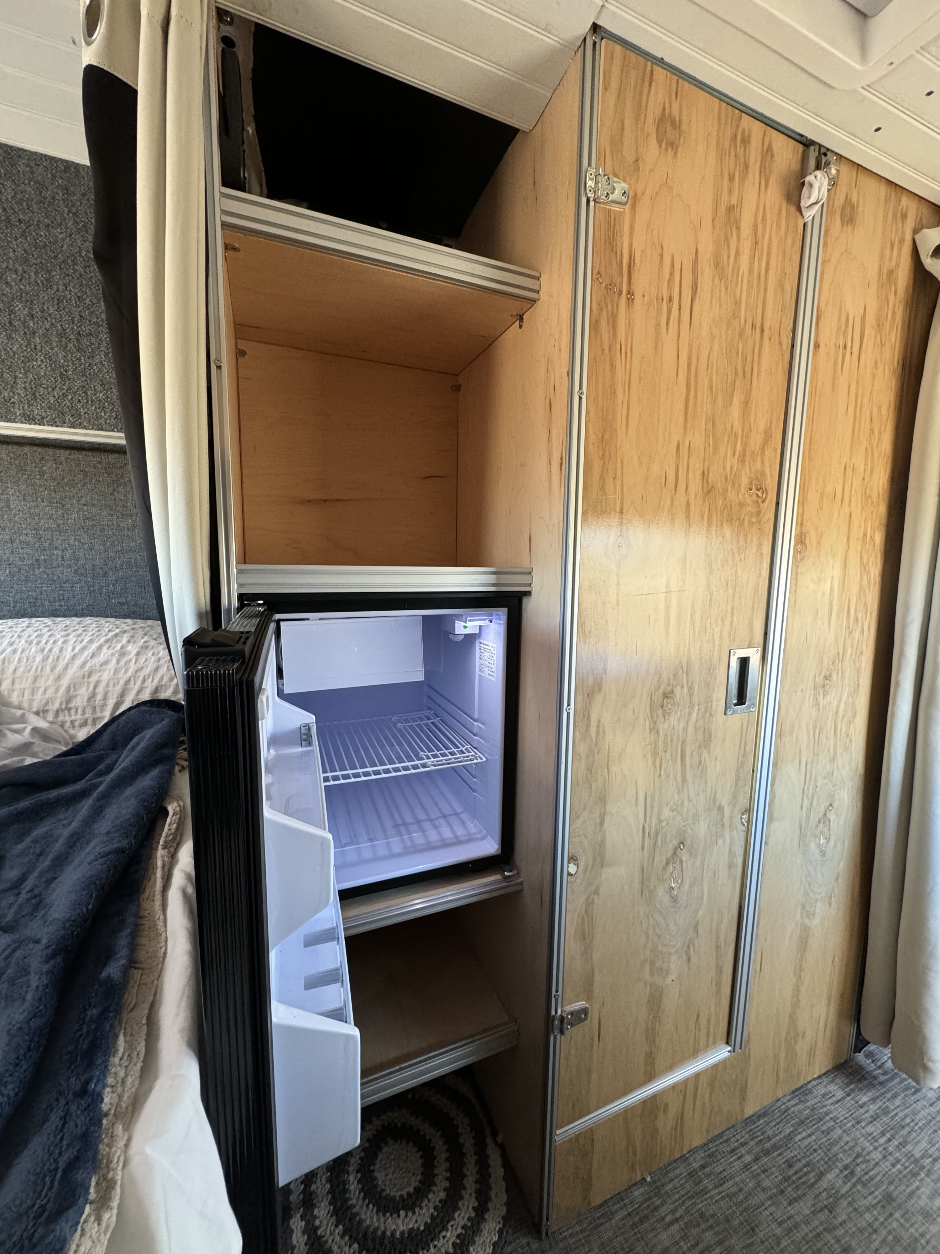 Inside an RV rental: compact fridge, open shelving, and wood-paneled storage. Essential for camper van life.. Ford Transit 2015