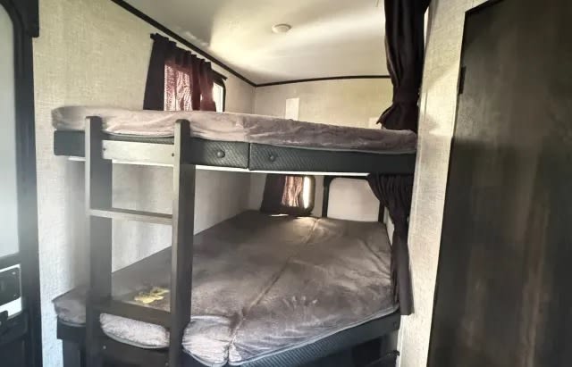Interior of an rv rental showcasing a set of bunk beds with a ladder, dark frames, and light bedding.. Jayco White Hawk 2023